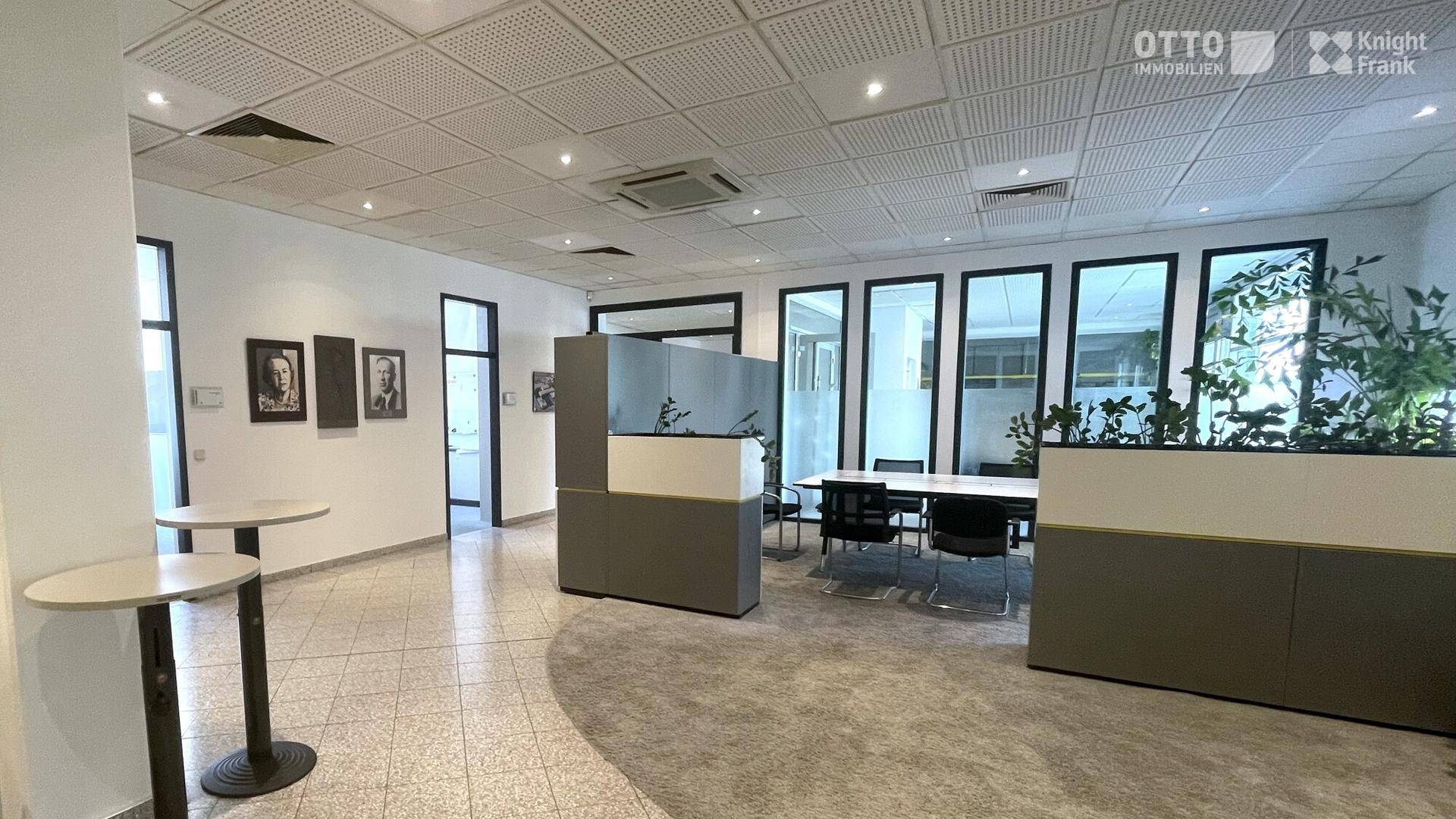 Moderner Bürobereich mit gefliestem Boden, großen Fenstern und Trennwänden für Besprechungen.