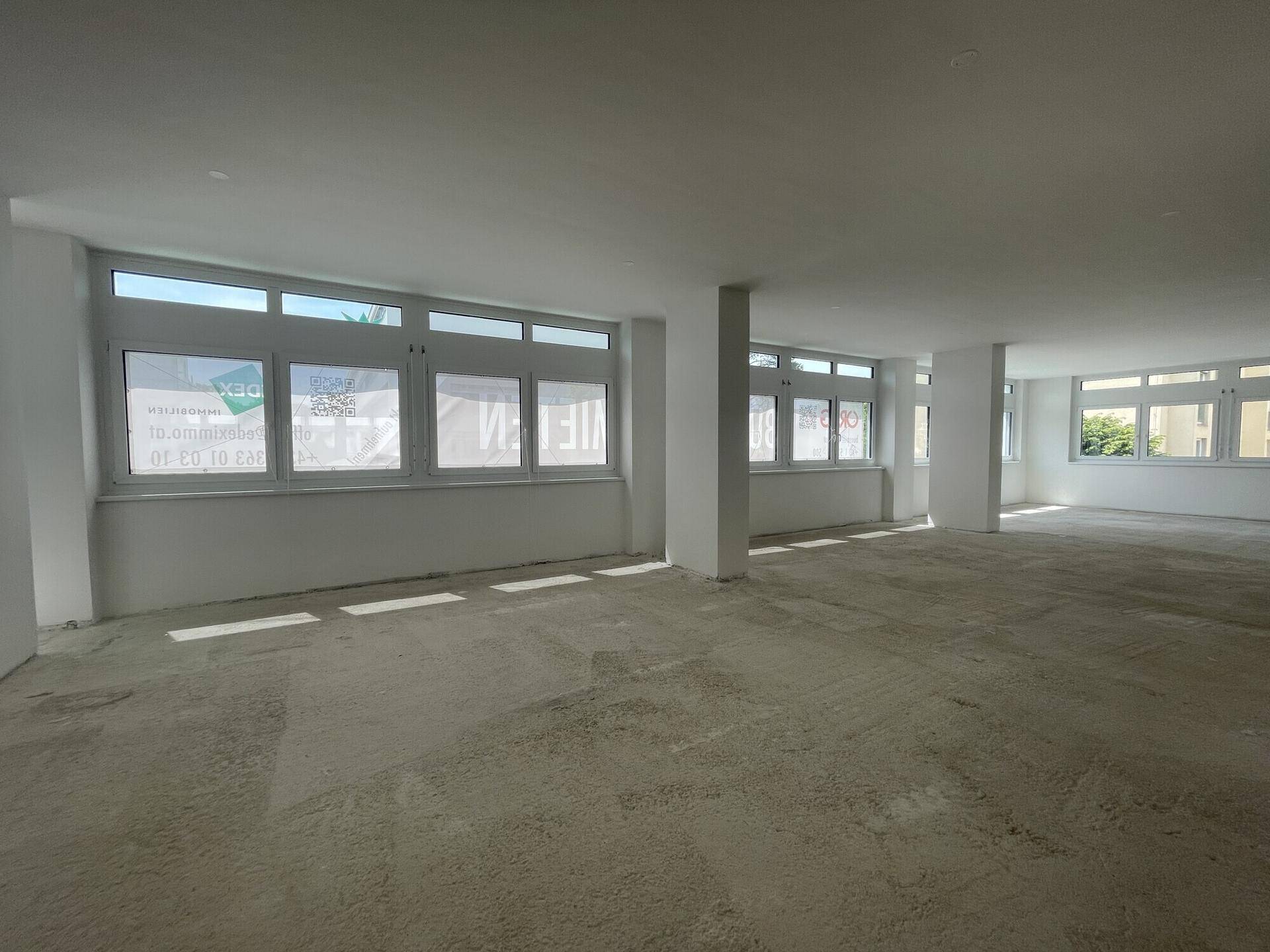 Großer, heller Büroraum mit vielen Fenstern und Betonboden, bereit für die individuelle Gestaltung und Nutzung.