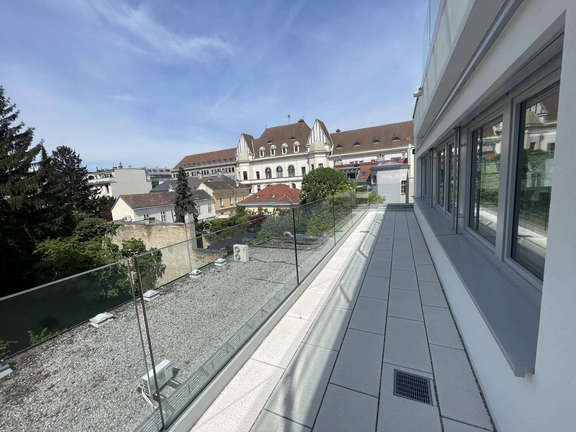 Lange Terrasse mit Glasgeländer und Blick auf die Stadt und grüne Umgebung.
