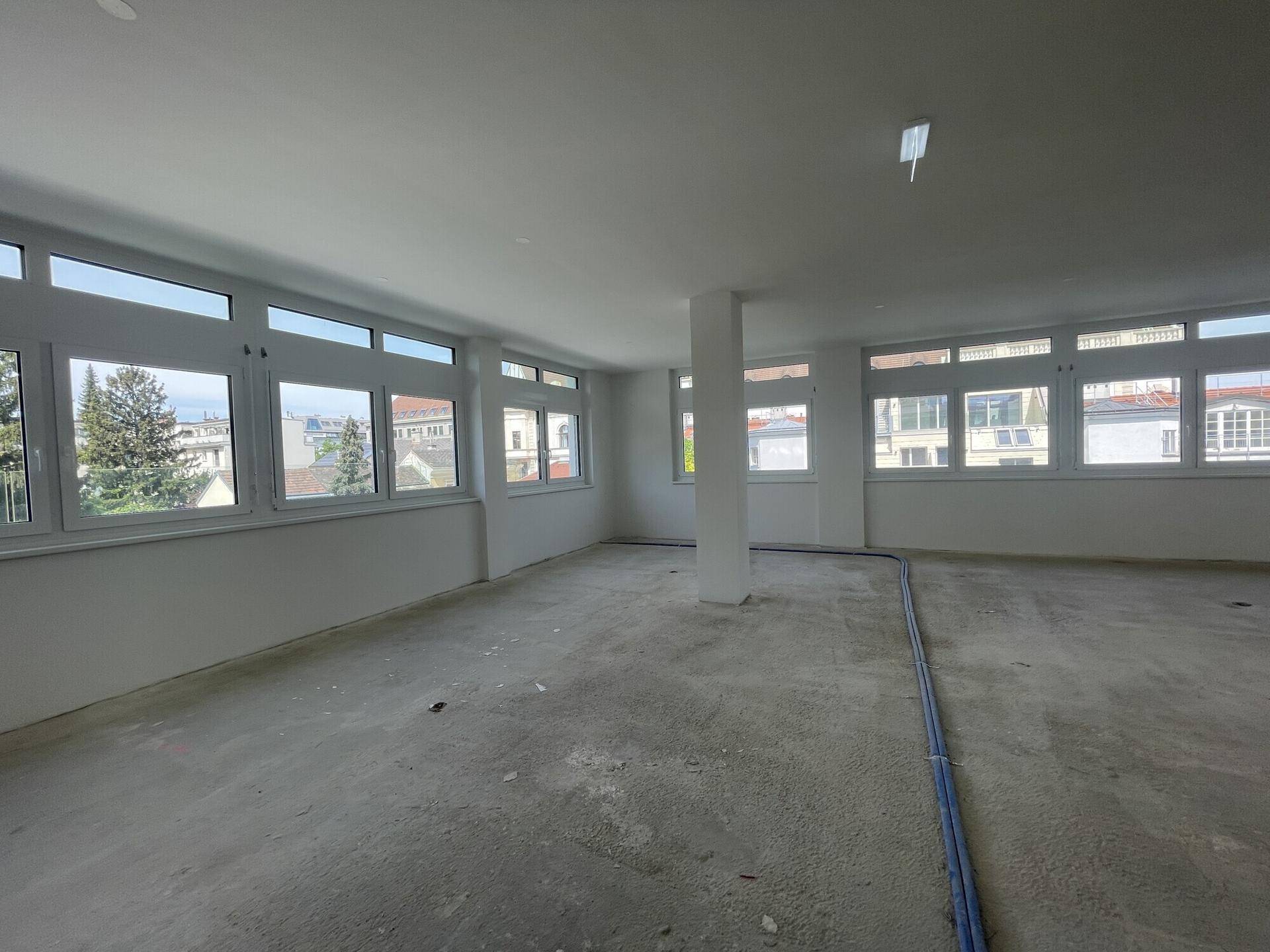 Heller Büroraum mit Säulen und blauen Leitungen auf dem Betonboden, bereit zum Ausbau.