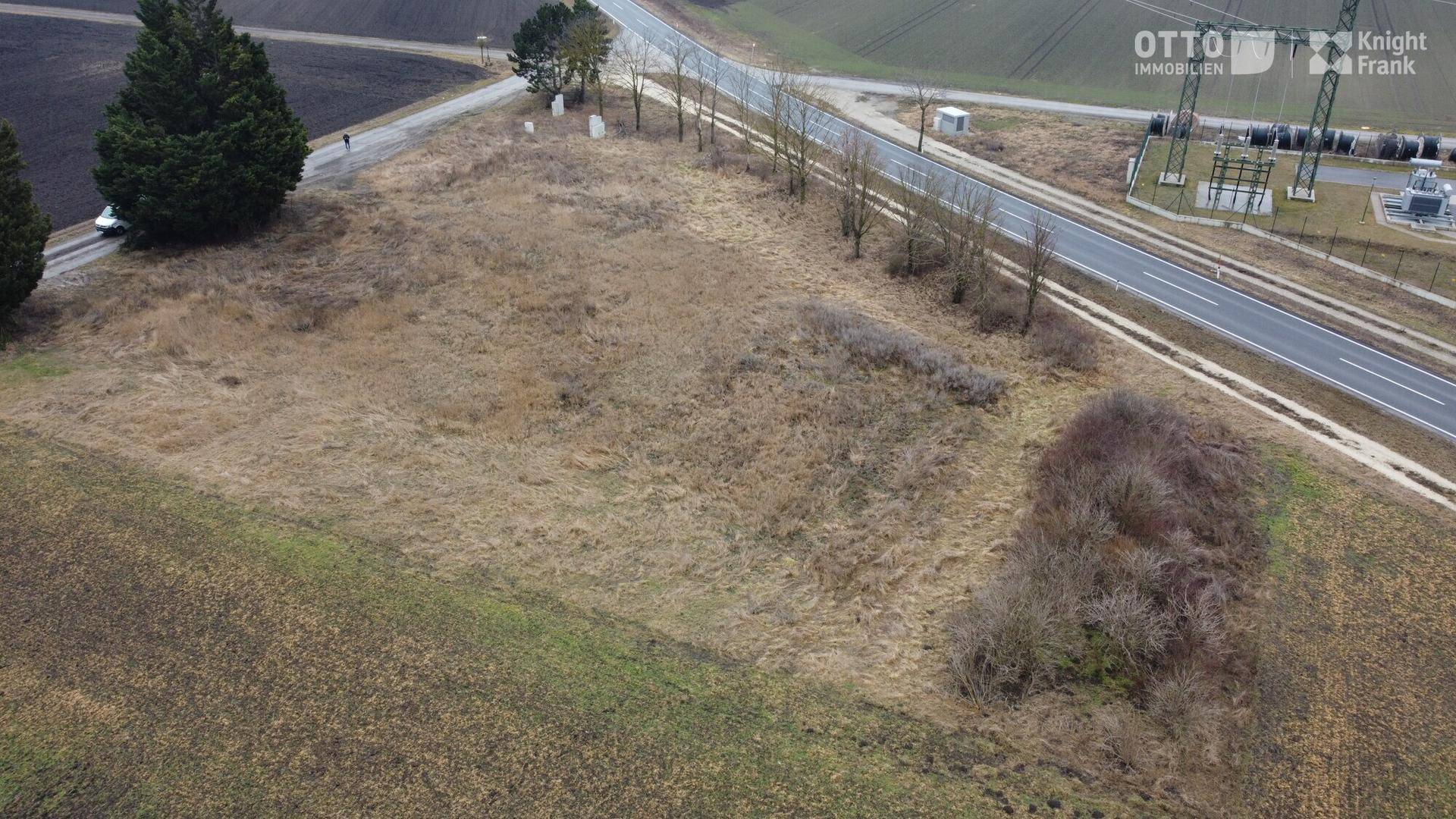 Luftaufnahme eines Grundstücks mit trockener Vegetation neben einer Straße und einer Stromanlage.