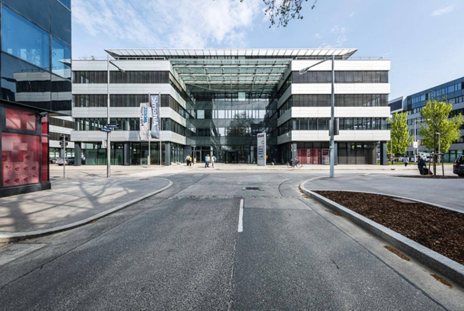 Eingangsbereich eines modernen Bürokomplexes mit Glasdach und breiter Zufahrt.