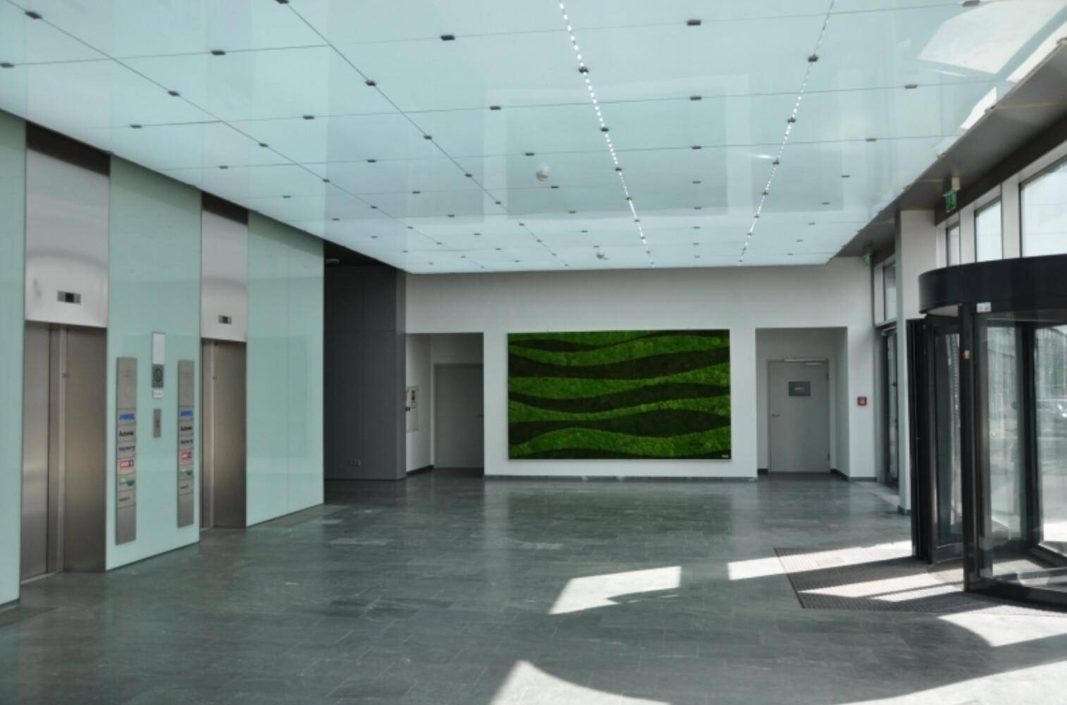 Helle und moderne Lobby mit Aufzügen, Drehtür und einer grünen Mooswand.
