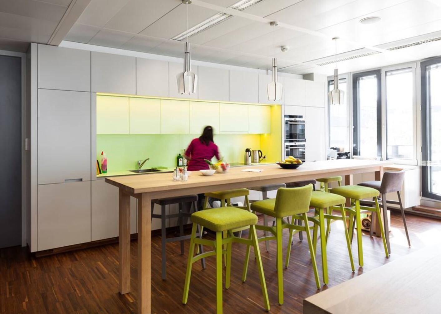 Moderne Büroküche mit Holzboden, langer Theke und hellgrünen Akzenten.