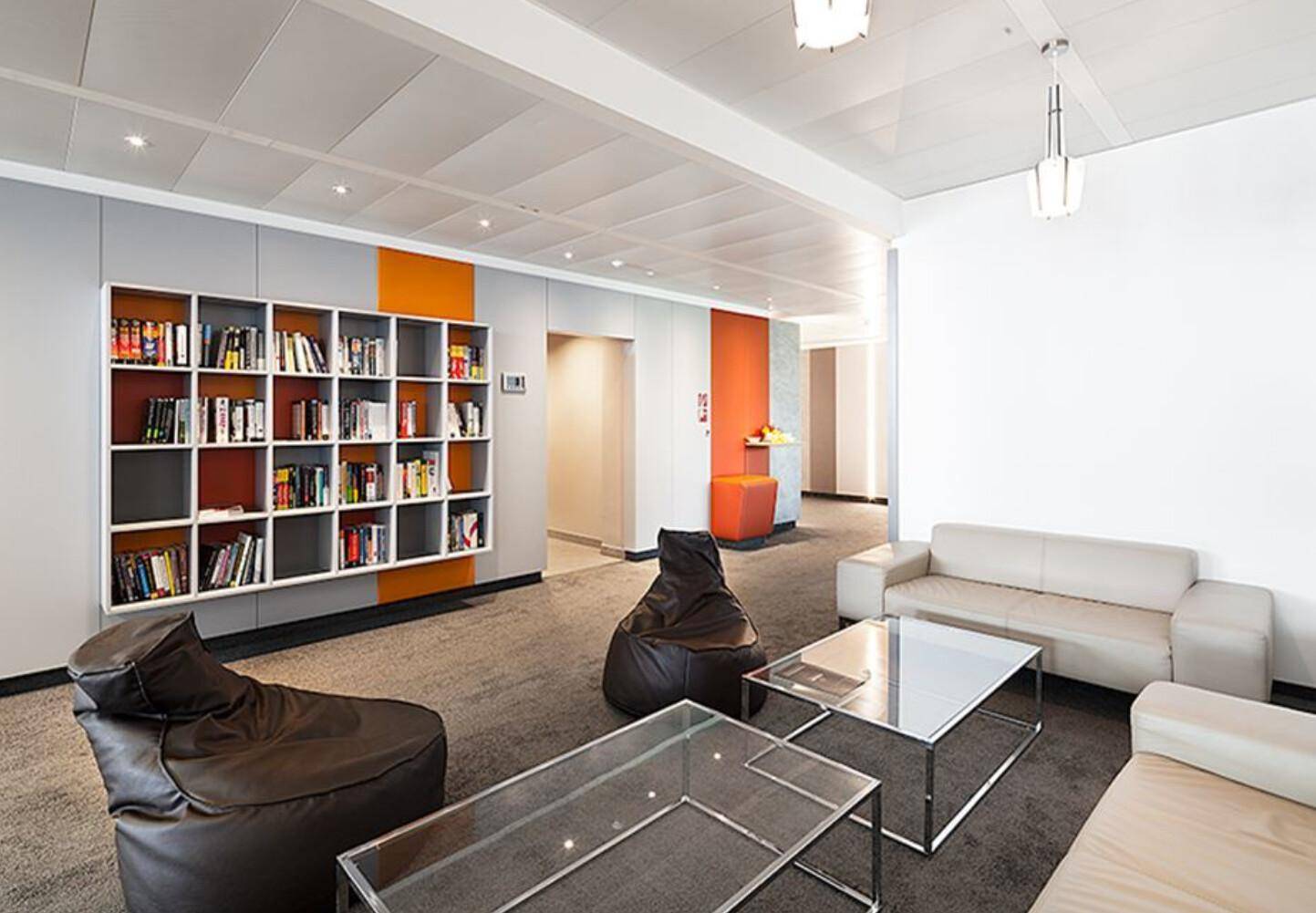 Gemütlicher Loungebereich mit Sofas, Sitzsäcken und einem Bücherregal in modernen Farben.