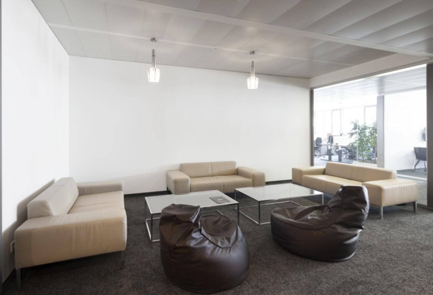 Heller Loungebereich mit beigen Sofas, Glastischen und dunklem Teppichboden.
