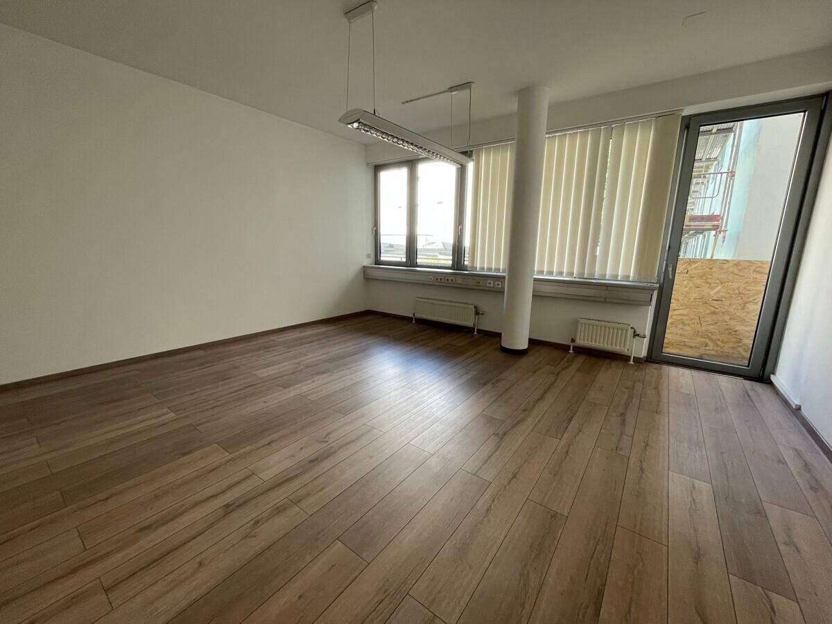 Geräumiges Büro mit modernem Laminatboden, großen Fenstern und Zugang zu einem Außenbereich.