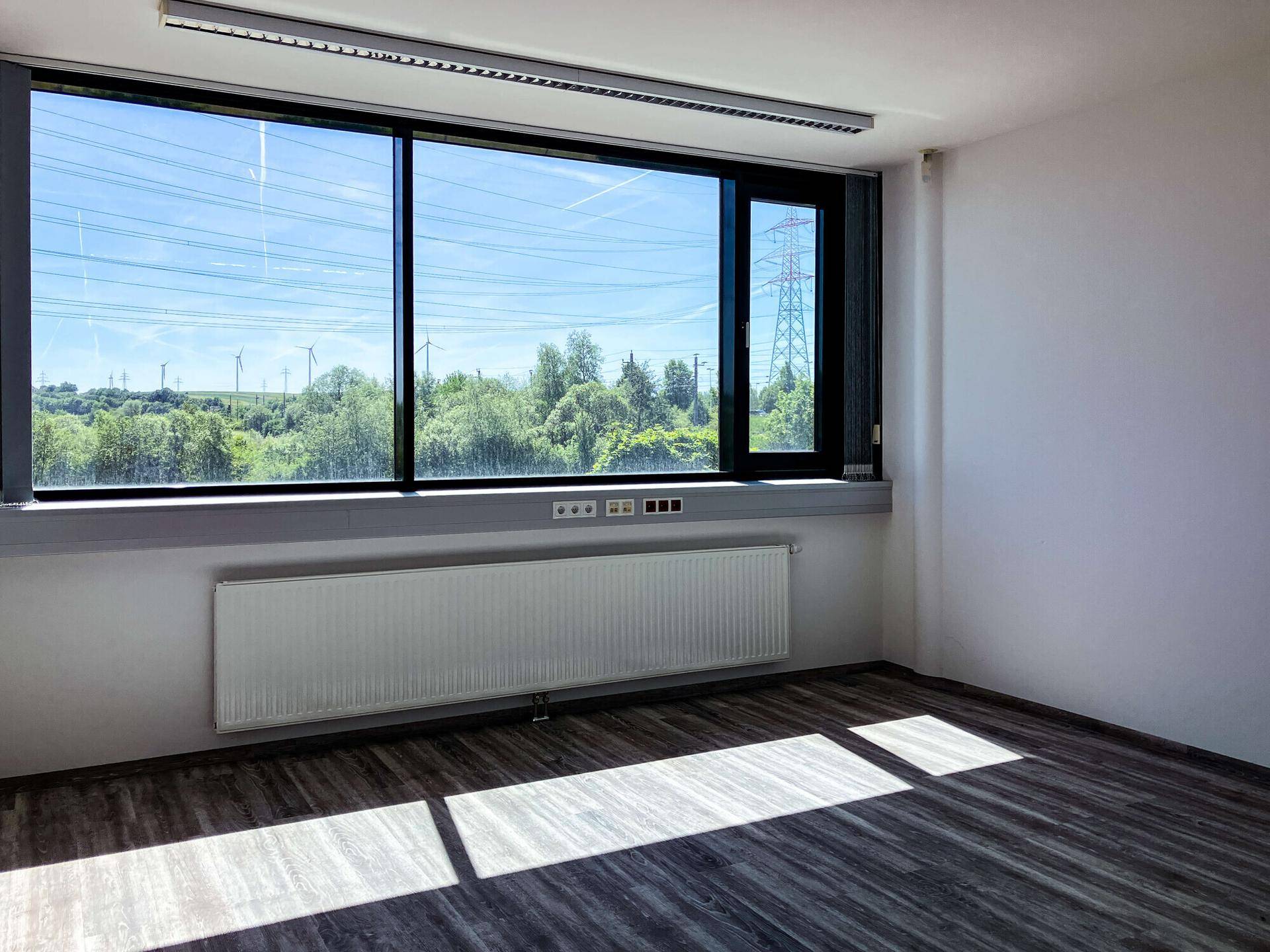 Leeres Büro mit großem Fenster, das viel Tageslicht und eine weite Aussicht bietet.