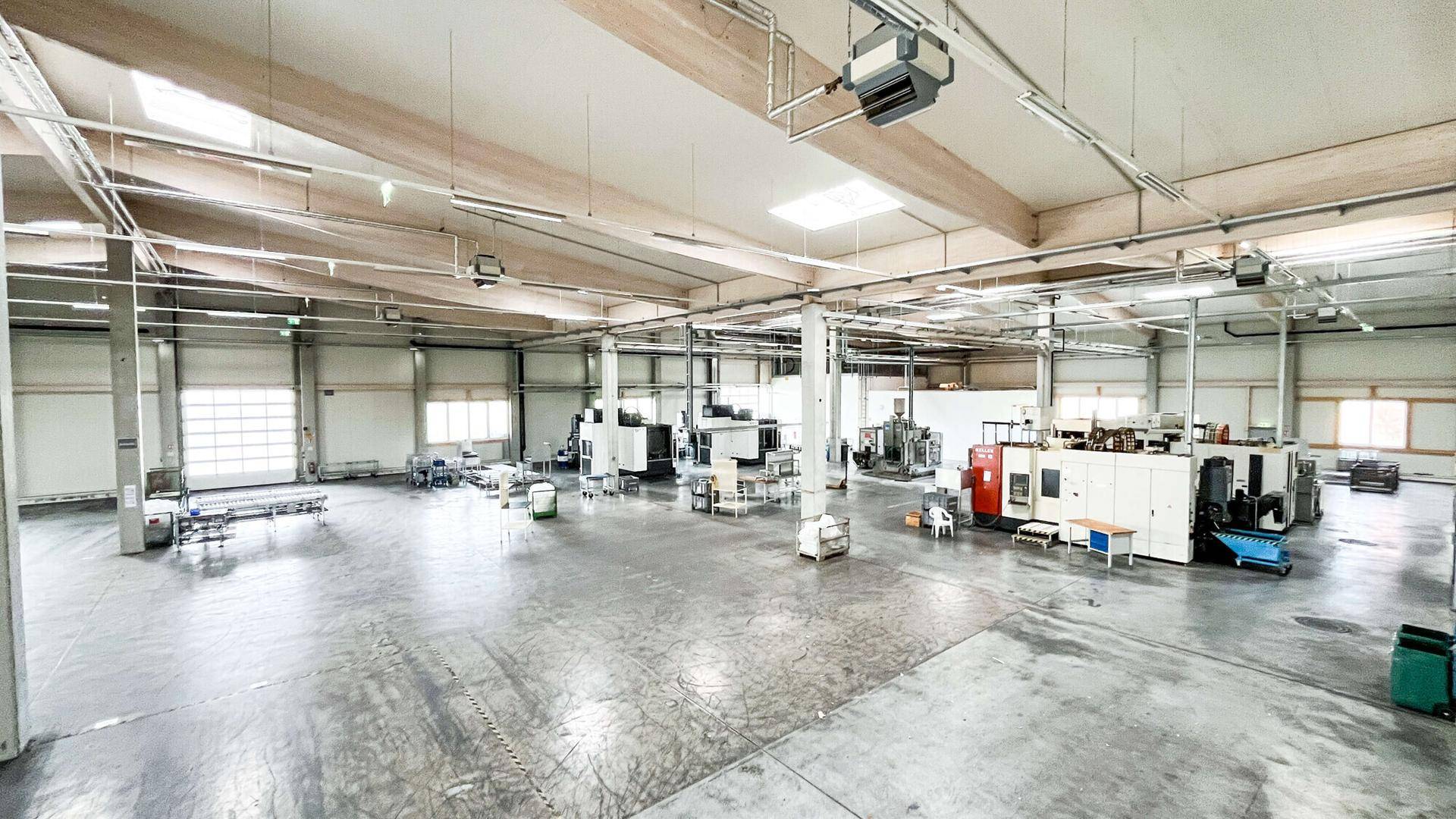 Große Produktionshalle mit Maschinen, hohen Decken und viel Tageslicht durch Oberlichter.