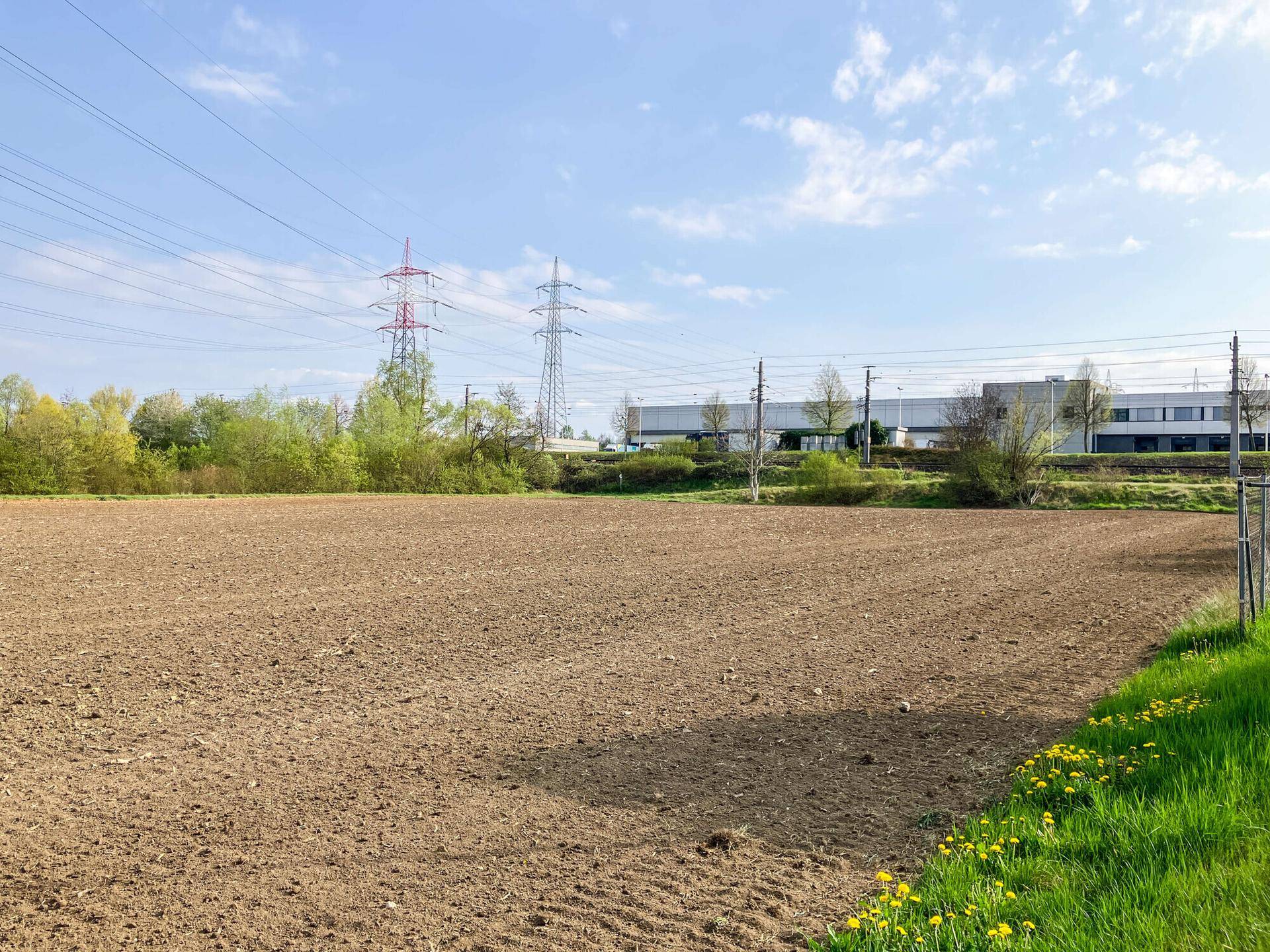 Weitläufiges, unbebautes Feld neben dem Grundstück mit Stromleitungen im Hintergrund.