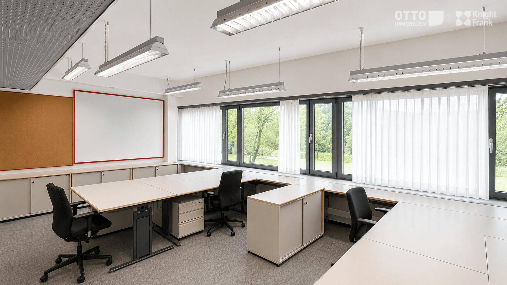 Helles Büro mit großen Fenstern, Jalousien und mehreren Arbeitsplätzen.