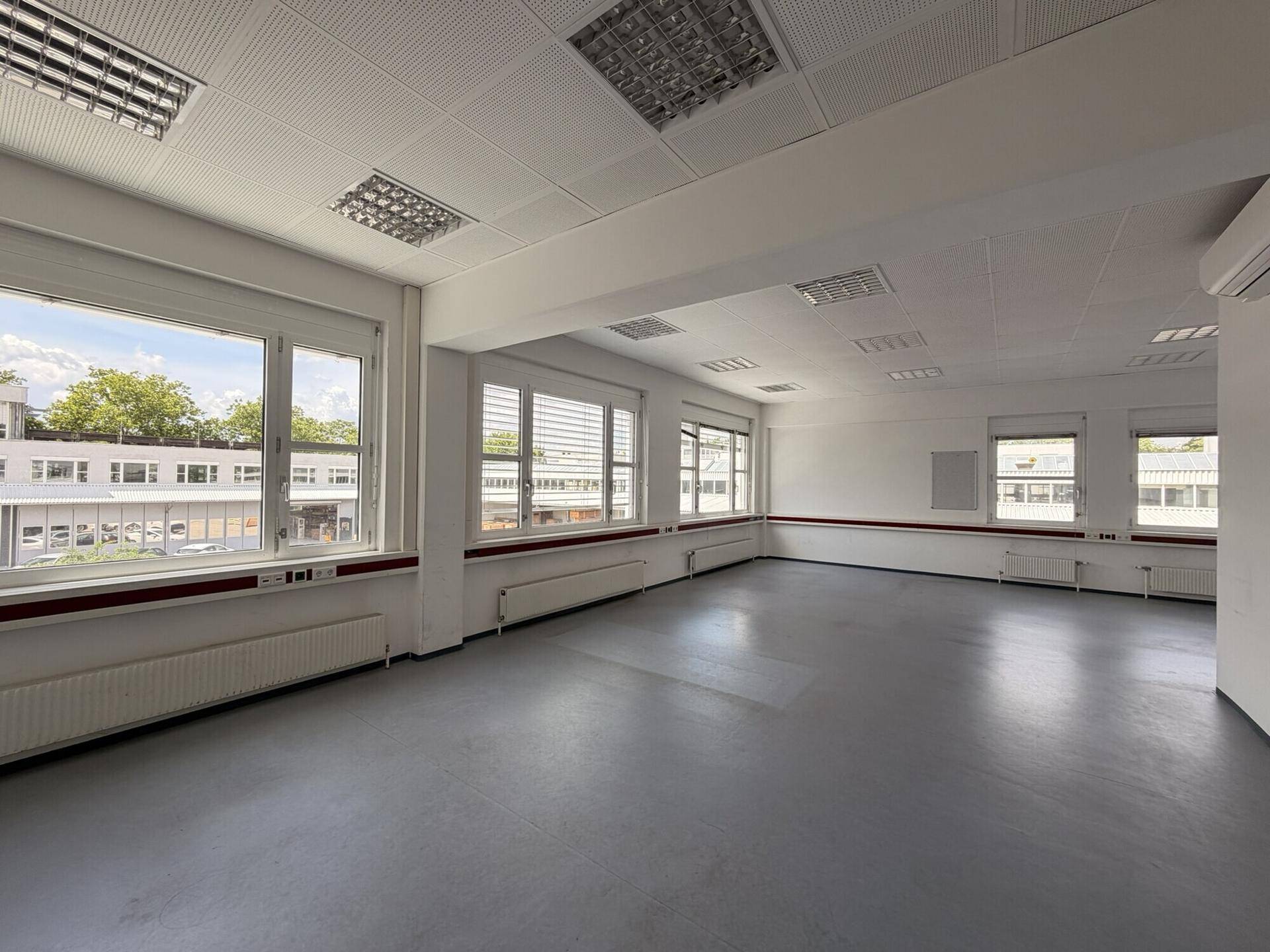 Großes, leeres Büro mit vielen Fenstern, die eine weite Aussicht auf die Umgebung ermöglichen und eine Klimaanlage.