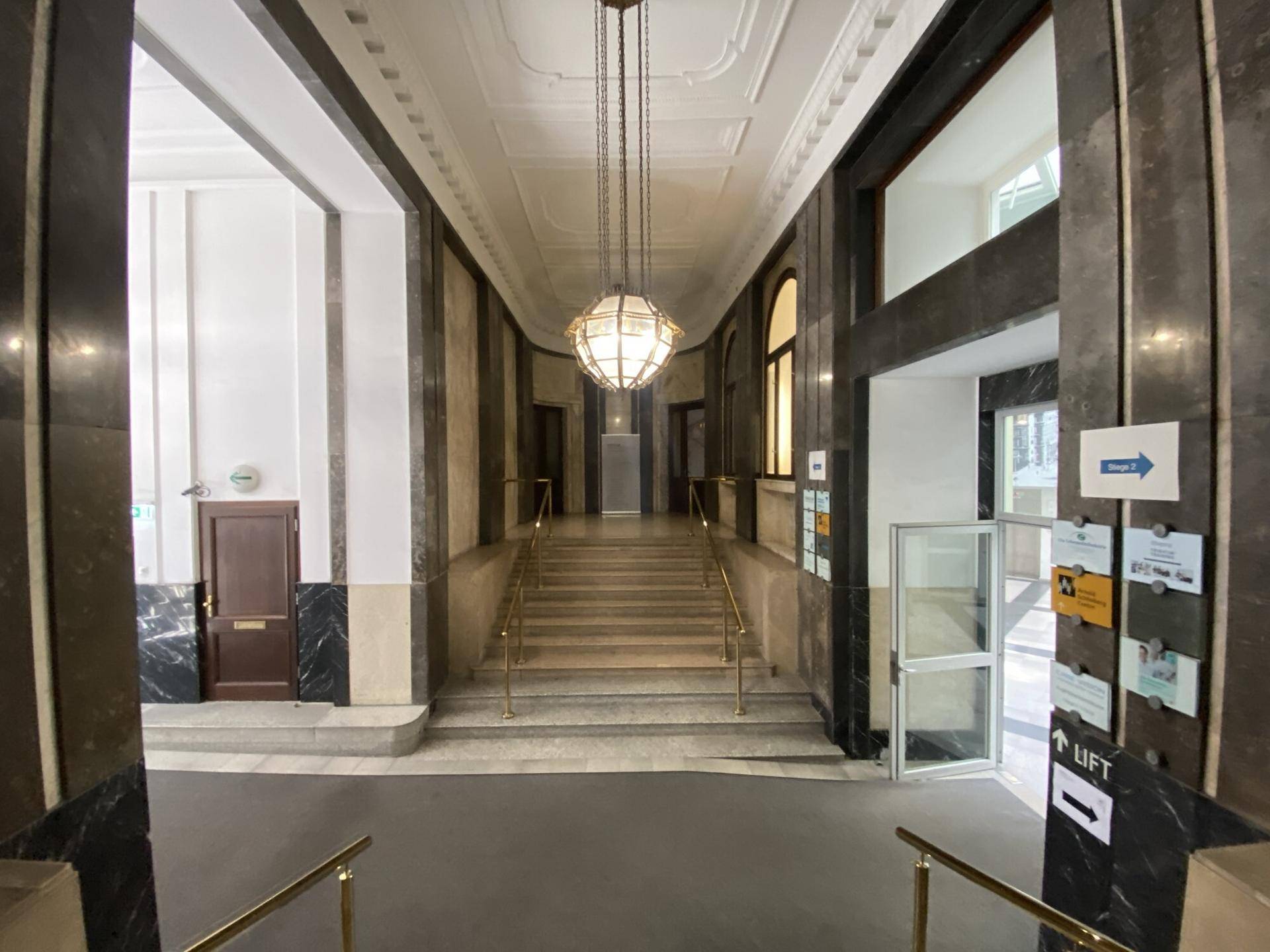 Elegantes Foyer mit Marmorwänden, breiter Treppe und einem auffälligen Kronleuchter, inklusive Liftzugang.