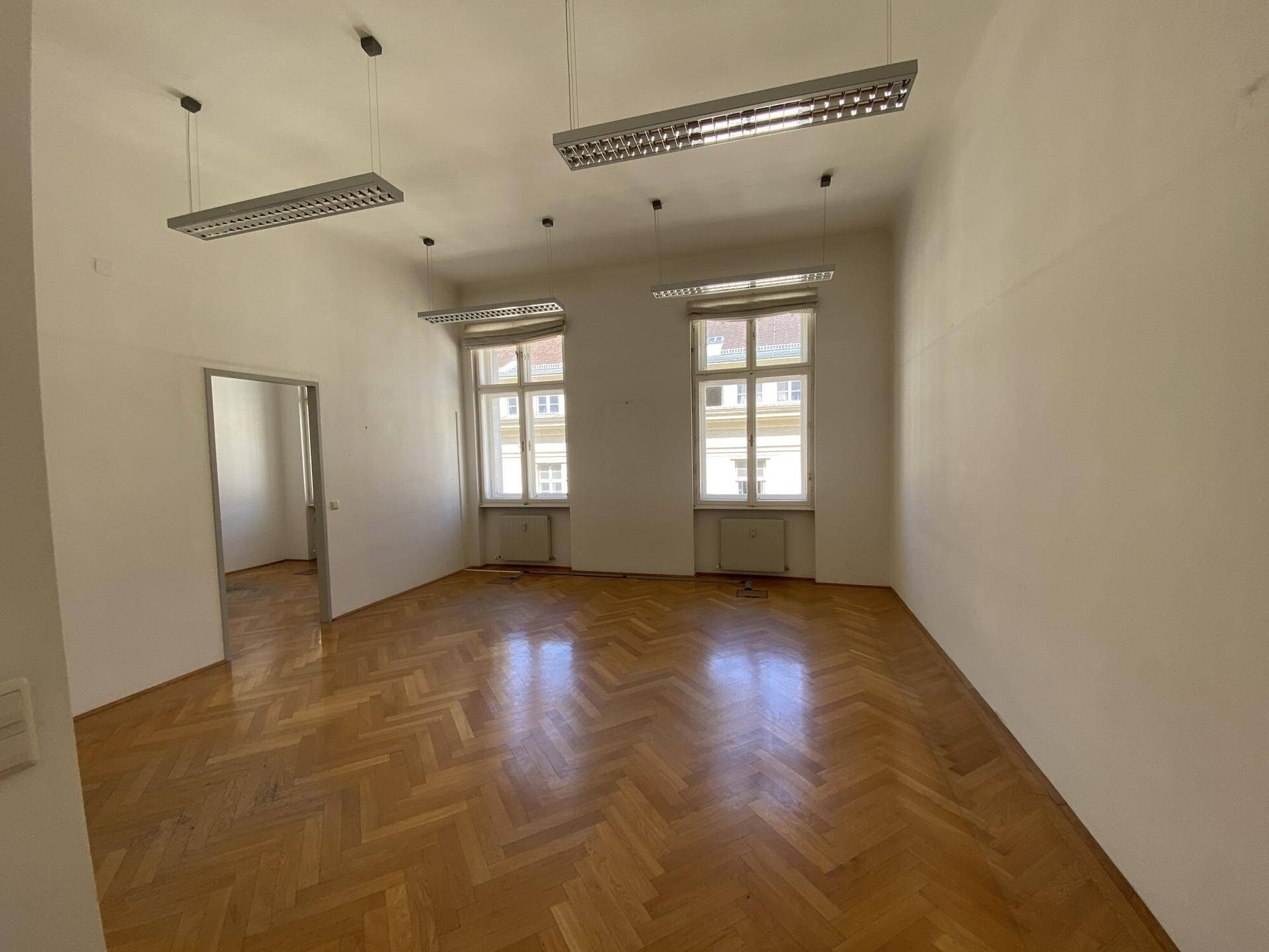 Helles Büro mit Fischgrätparkett und Zugang zu einem weiteren Raum, ideal für flexible Nutzung.