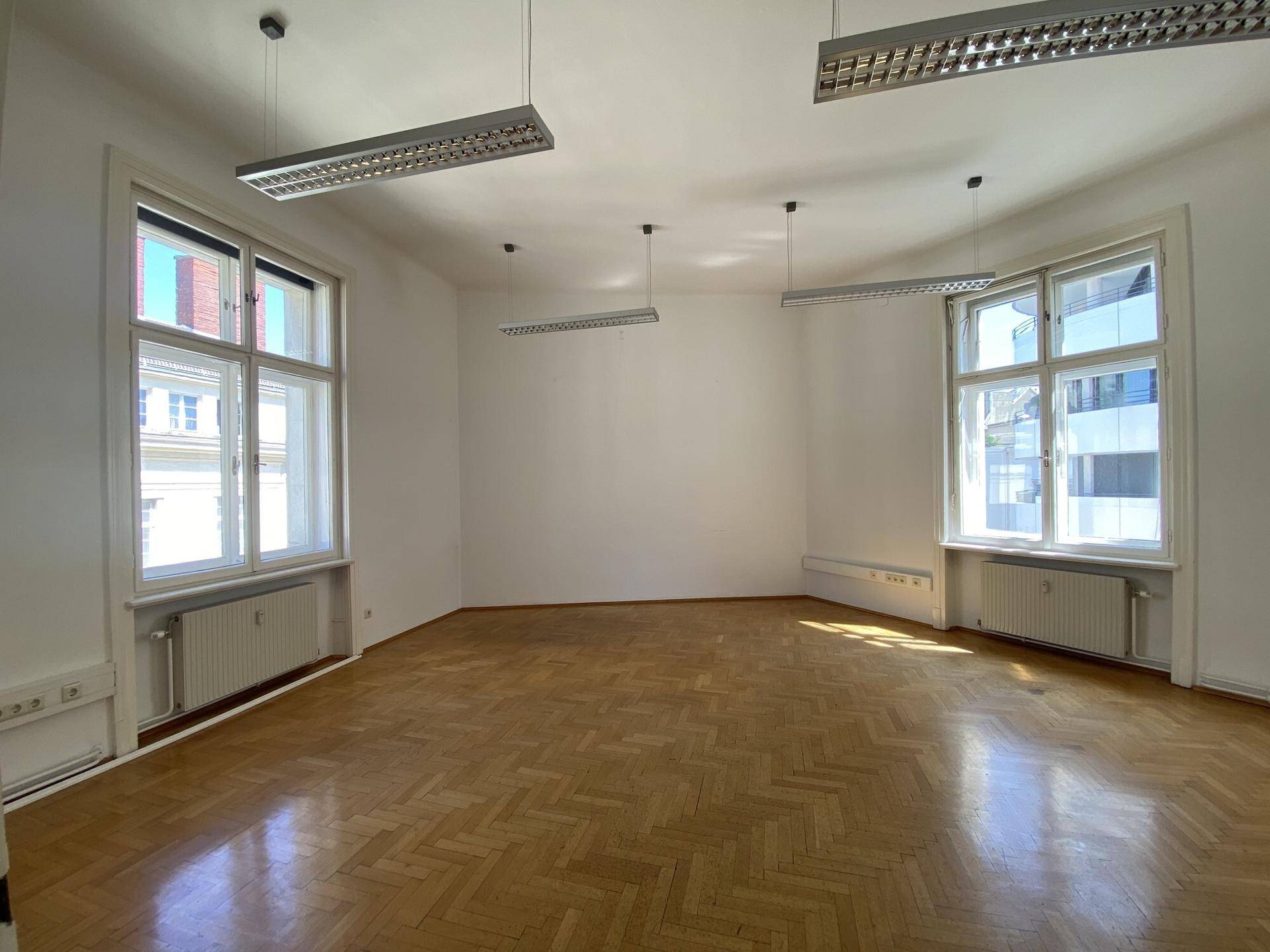 Leeres Büro mit Fischgrätparkett, zwei großen Fenstern und guter natürlicher Belichtung.