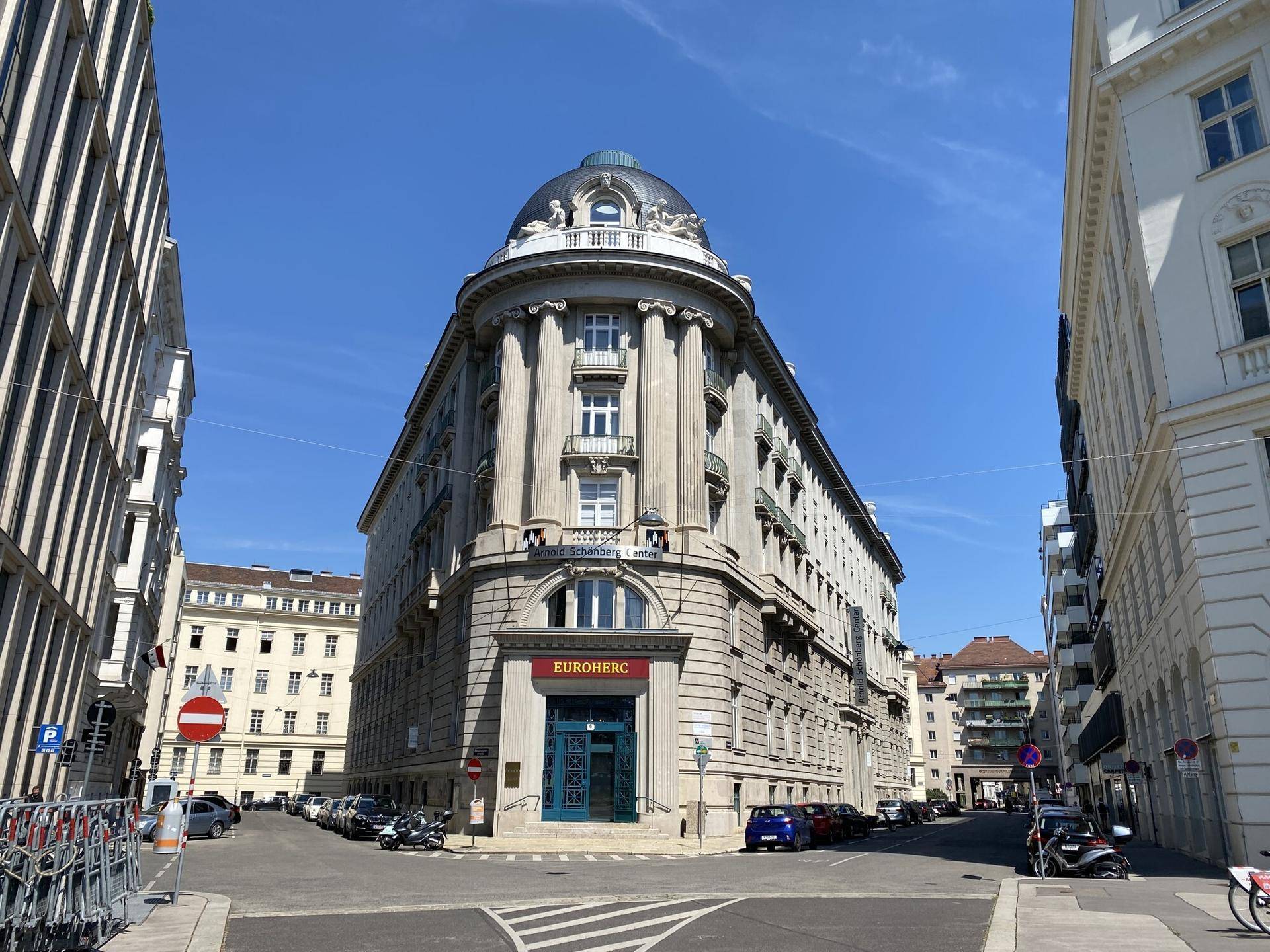 Prunkvolles Eckgebäude mit Kuppeldach und Säulen an einer städtischen Kreuzung, architektonisch beeindruckend.