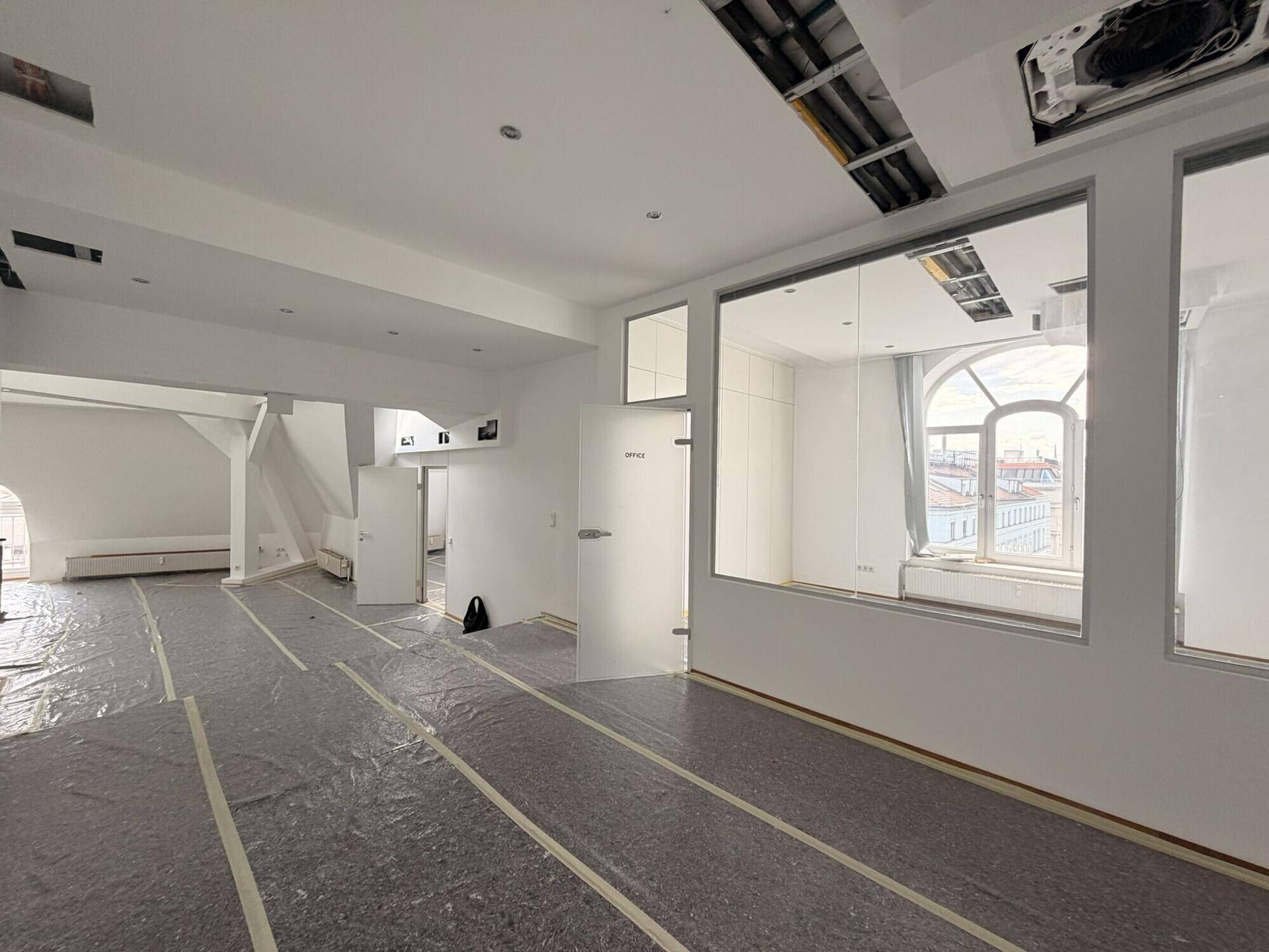 Großer, offener Bürobereich mit schrägen Decken und Blick auf einen angrenzenden Raum mit Rundbogenfenster.