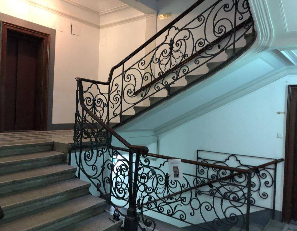 Historisches Treppenhaus mit kunstvollem schmiedeeisernem Geländer, Steinstufen und einem Aufzug.