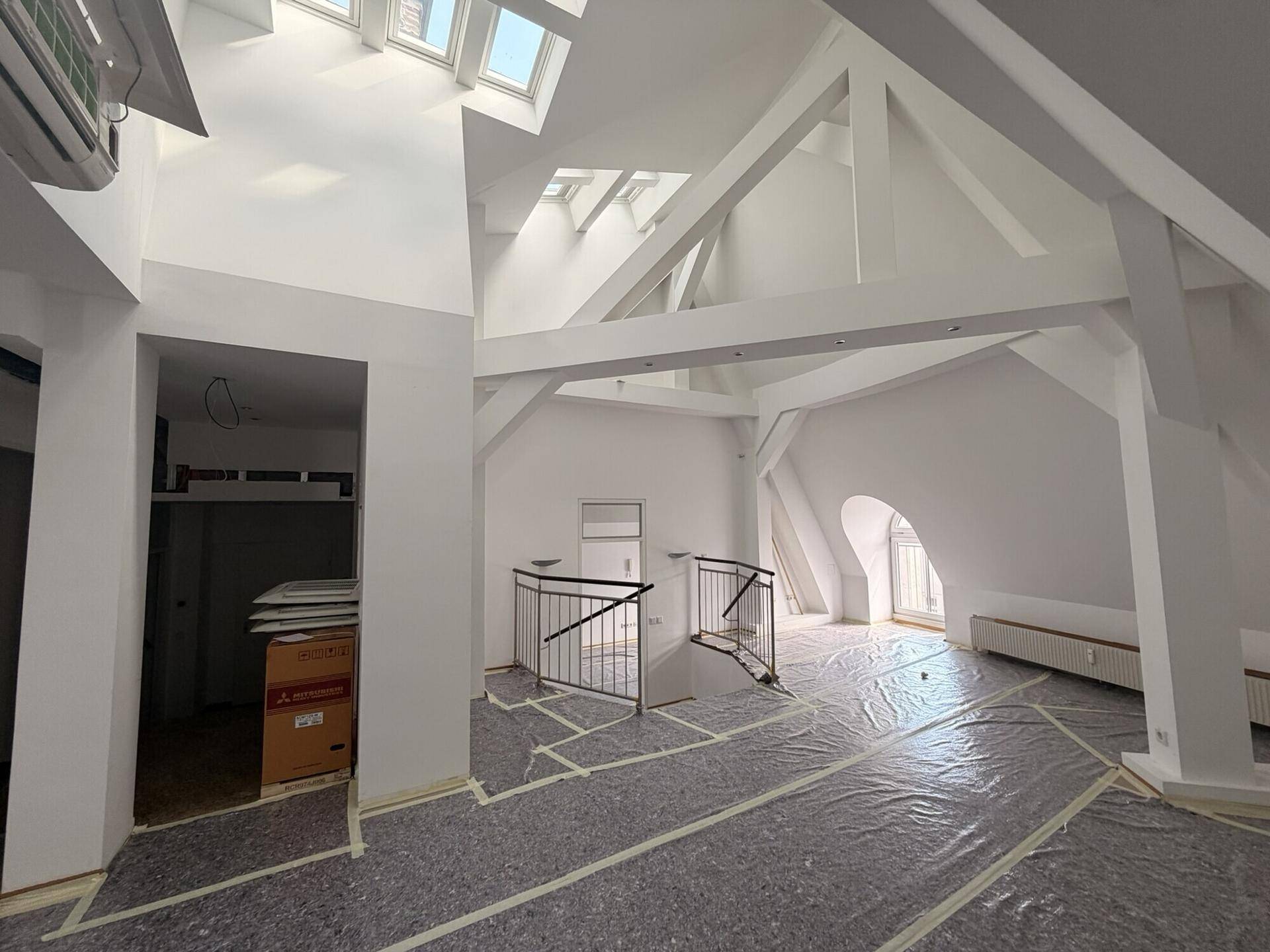 Weitläufiger Innenraum mit hohen, gewölbten Decken, sichtbaren Balken und mehreren Dachfenstern, in Renovierung.