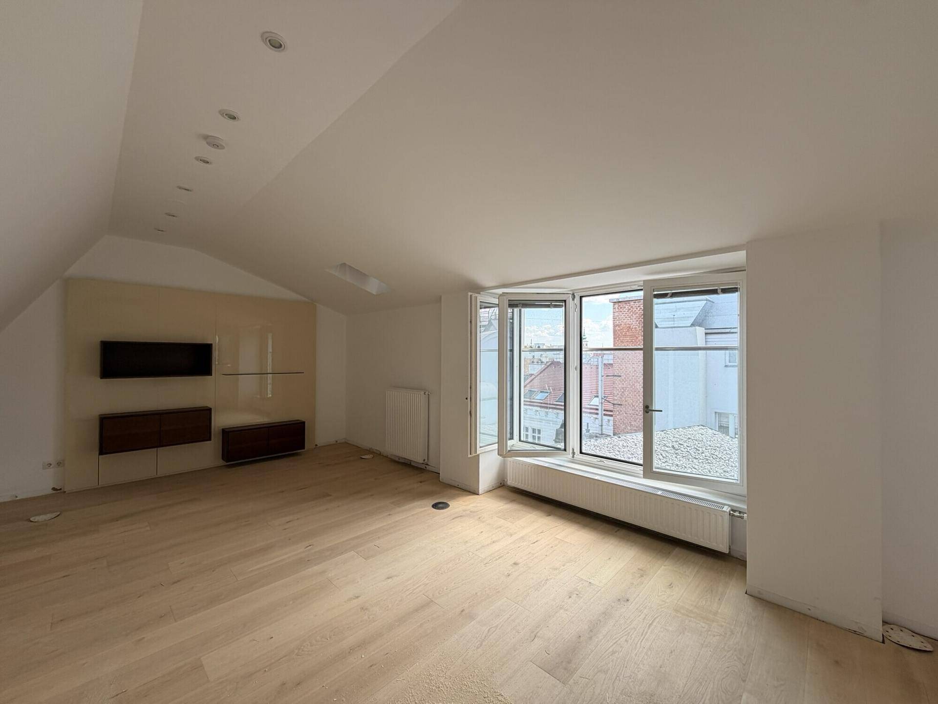 Heller Wohnraum mit hellem Holzboden, großem Erkerfenster und einer modernen Medieneinheit an der Wand.