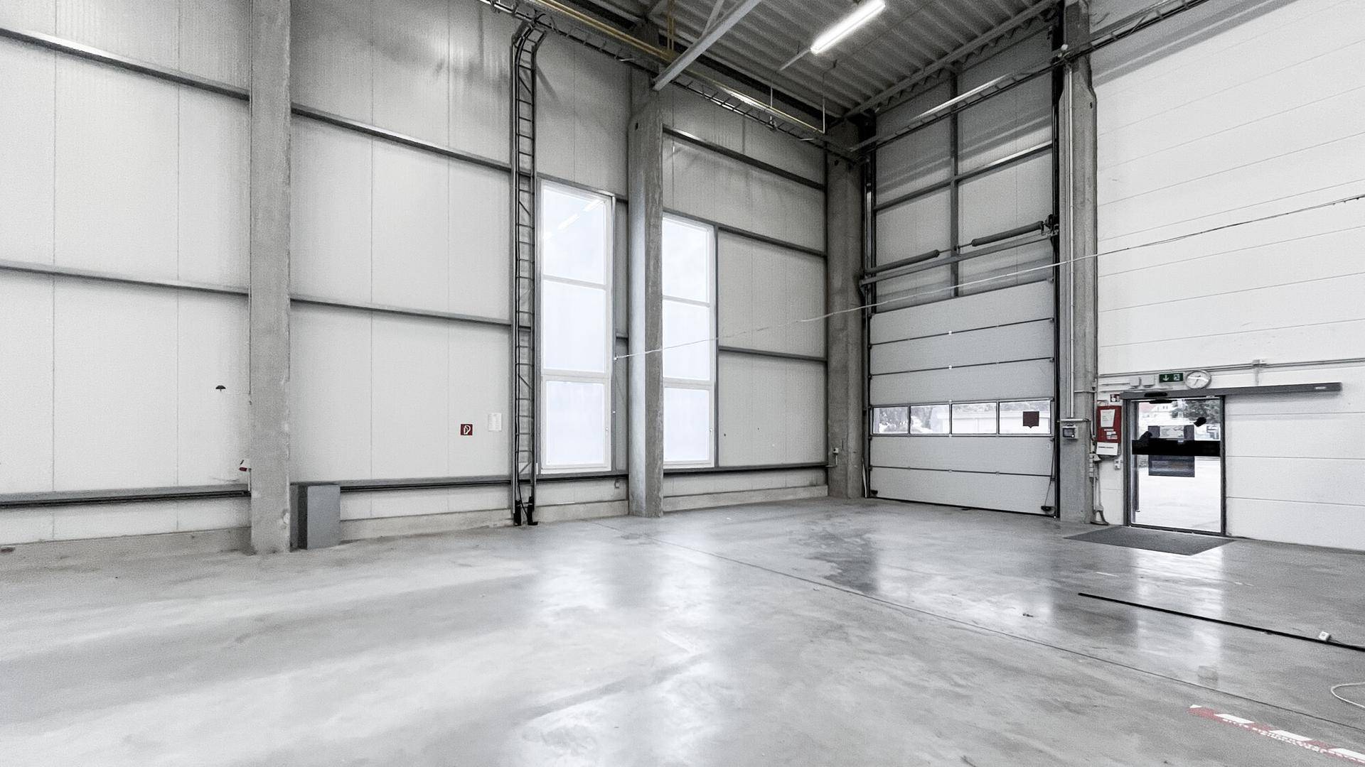 Große, helle Lagerhalle mit Betonboden, hohen Wänden und einem großen Rolltor für den Zugang.