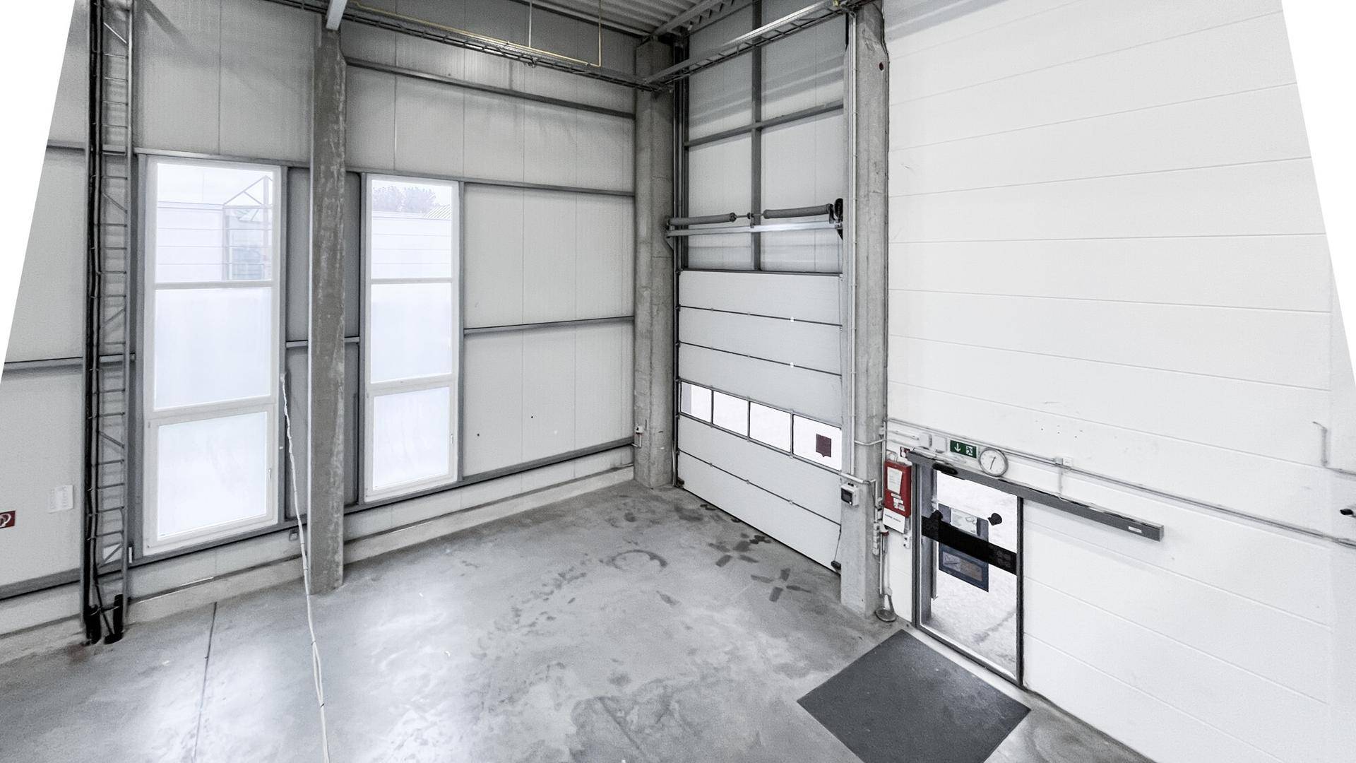 Eingangsbereich einer modernen Lagerhalle mit Rolltor, separater Tür und hohen Fenstern für Tageslicht.