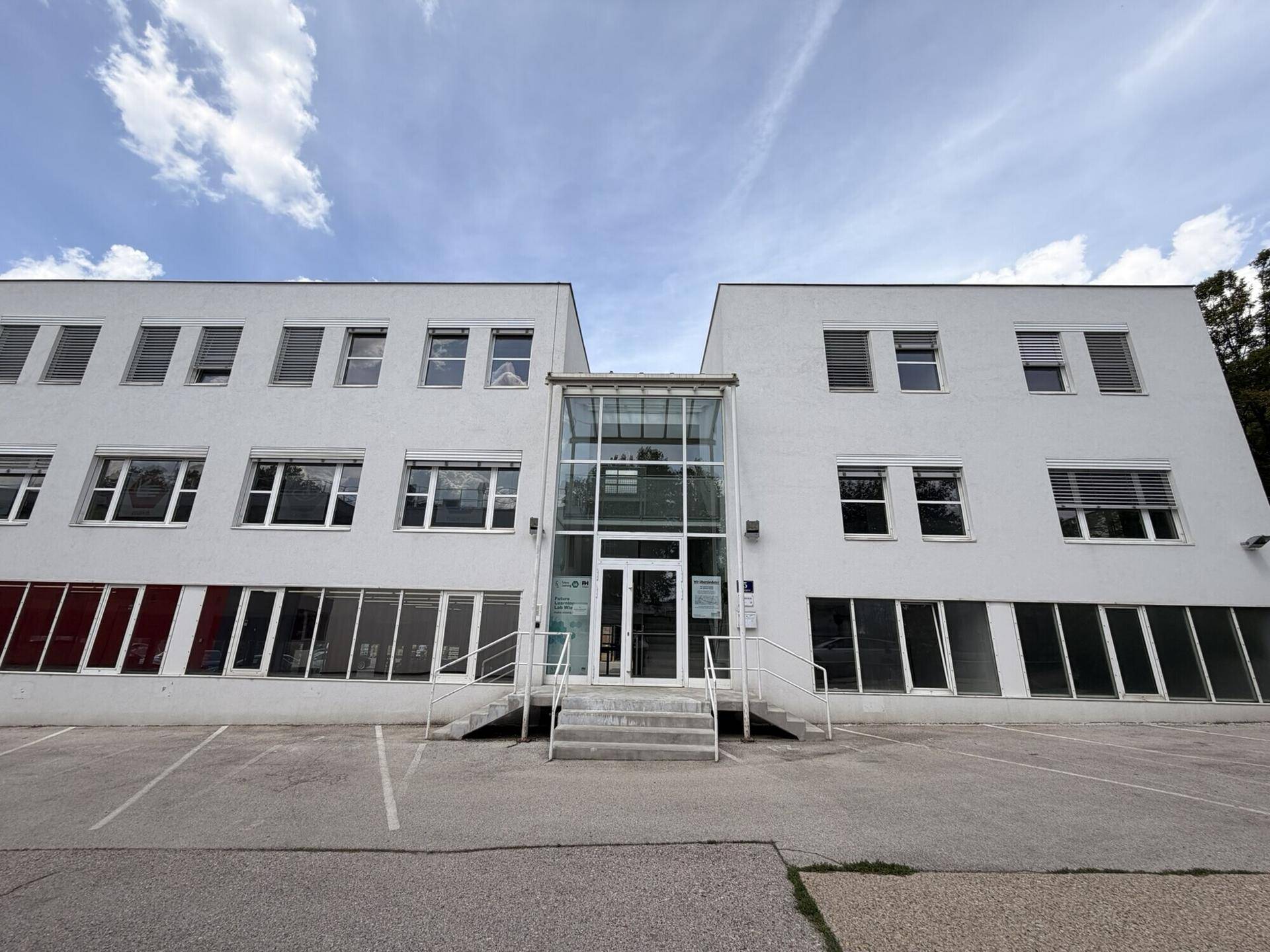 Modernes Bürogebäude mit weißer Fassade, großen Fenstern und einem gläsernen Eingangsbereich.