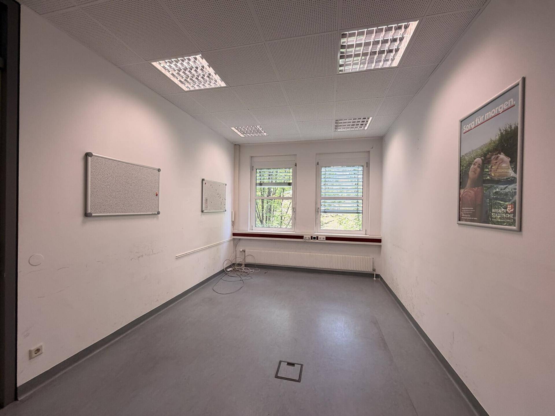 Kleineres Büro mit zwei Fenstern, die Tageslicht hereinlassen, und einer Pinnwand an der Wand.