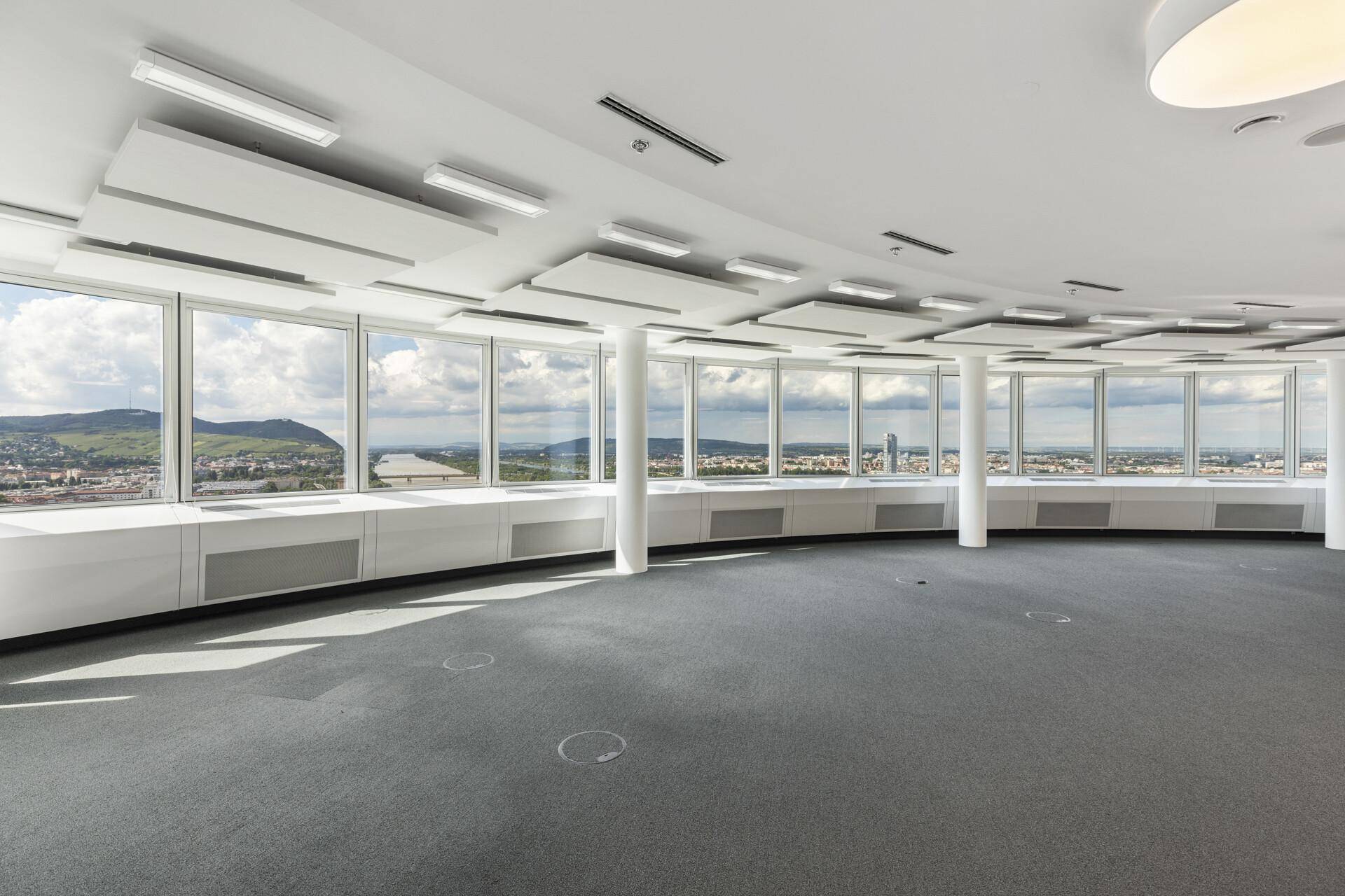 Großes, leeres Büro mit Teppichboden und einer Fensterfront, die eine weite Aussicht bietet.