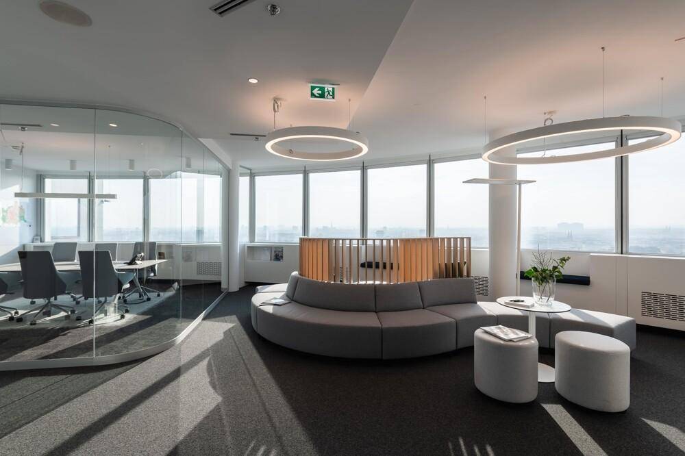 Offener Bürobereich mit runden Sofas, Besprechungsräumen und Panoramablick auf die Stadt.