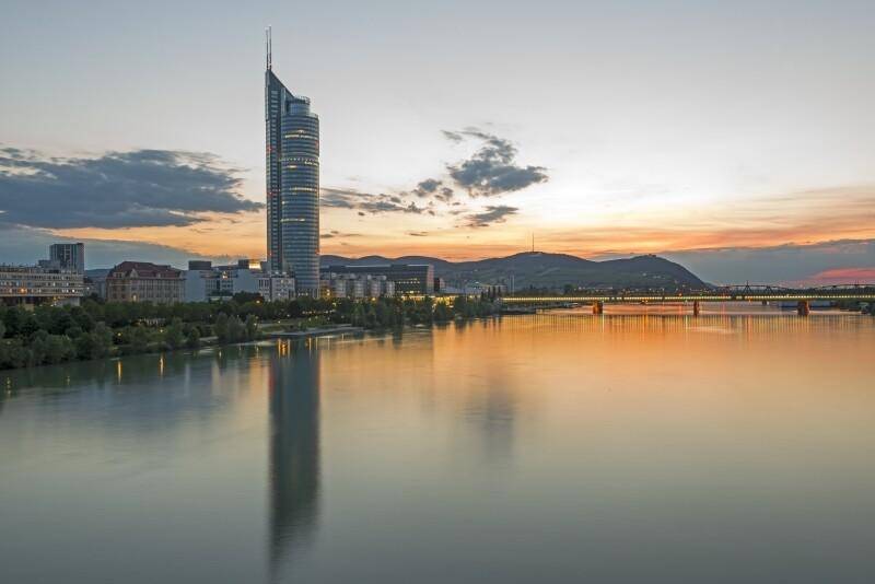 Beeindruckende Stadtansicht bei Sonnenuntergang mit einem markanten Wolkenkratzer am Flussufer.