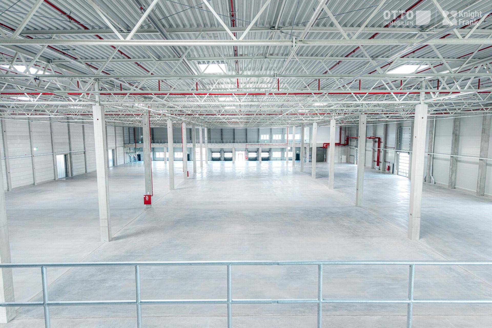 Weitläufige, leere Industriehalle aus erhöhter Perspektive, mit vielen Säulen und Laderampen im Hintergrund.