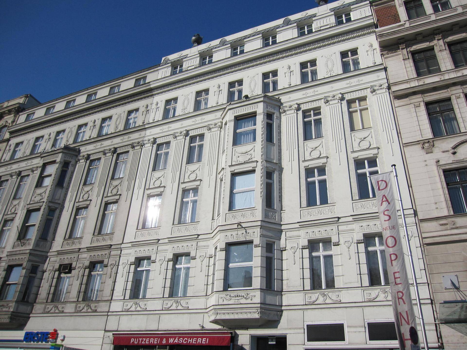 Historisches Gebäude mit reich verzierter weißer Fassade und vielen Fenstern unter blauem Himmel.
