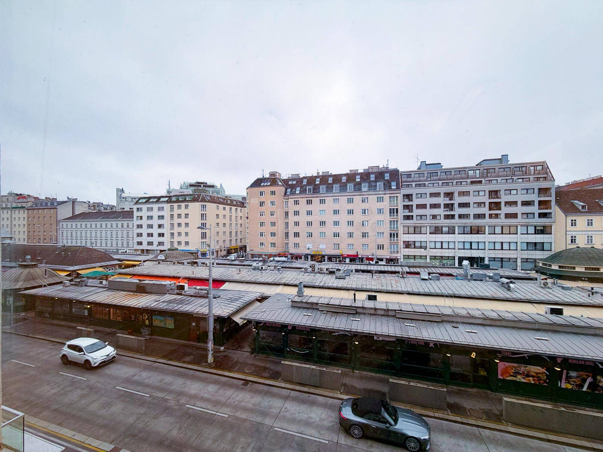 Blick aus dem Fenster auf eine belebte Stadtstraße mit Gebäuden und einem Marktbereich.