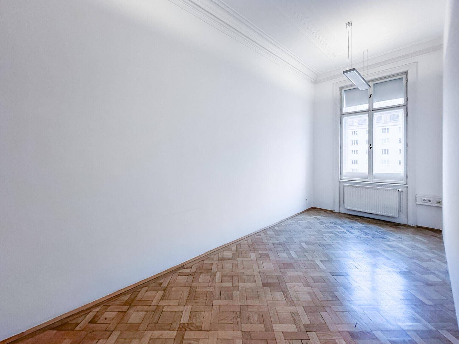 Heller, leerer Büroraum mit Fischgrätparkett und einem großen Fenster, ideal für Einzelbüro.