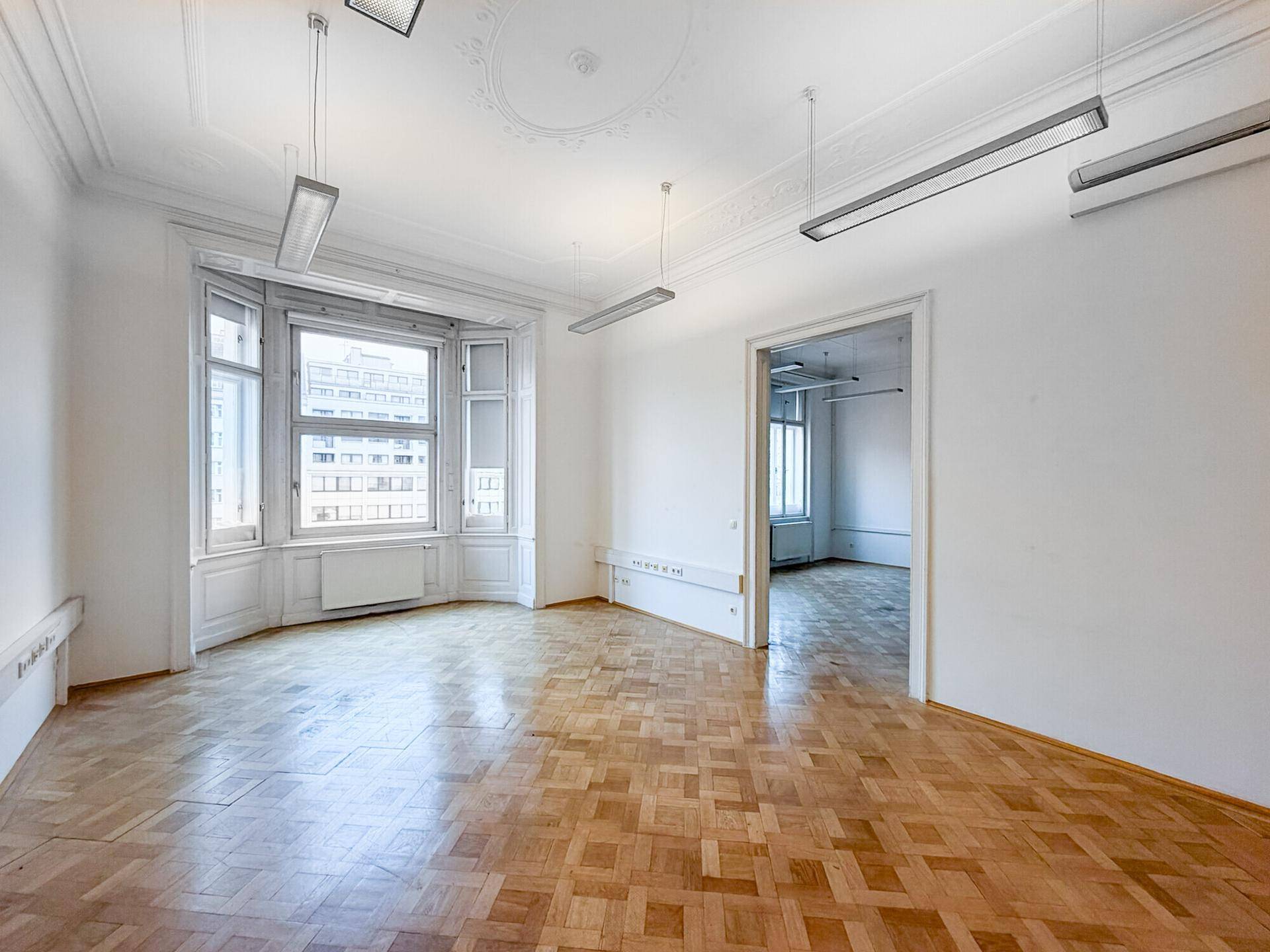 Helles, leeres Eckbüro mit Erkerfenster, Fischgrätparkett und hohen Decken.