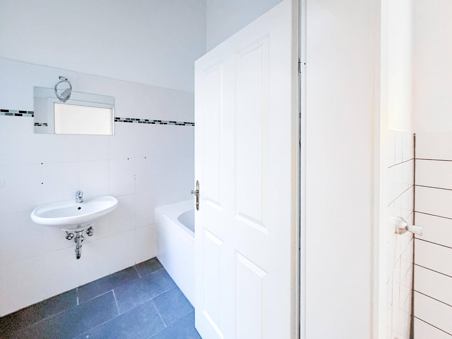 Badezimmer mit Badewanne, Waschbecken und kleinen Fliesenakzenten an der Wand.