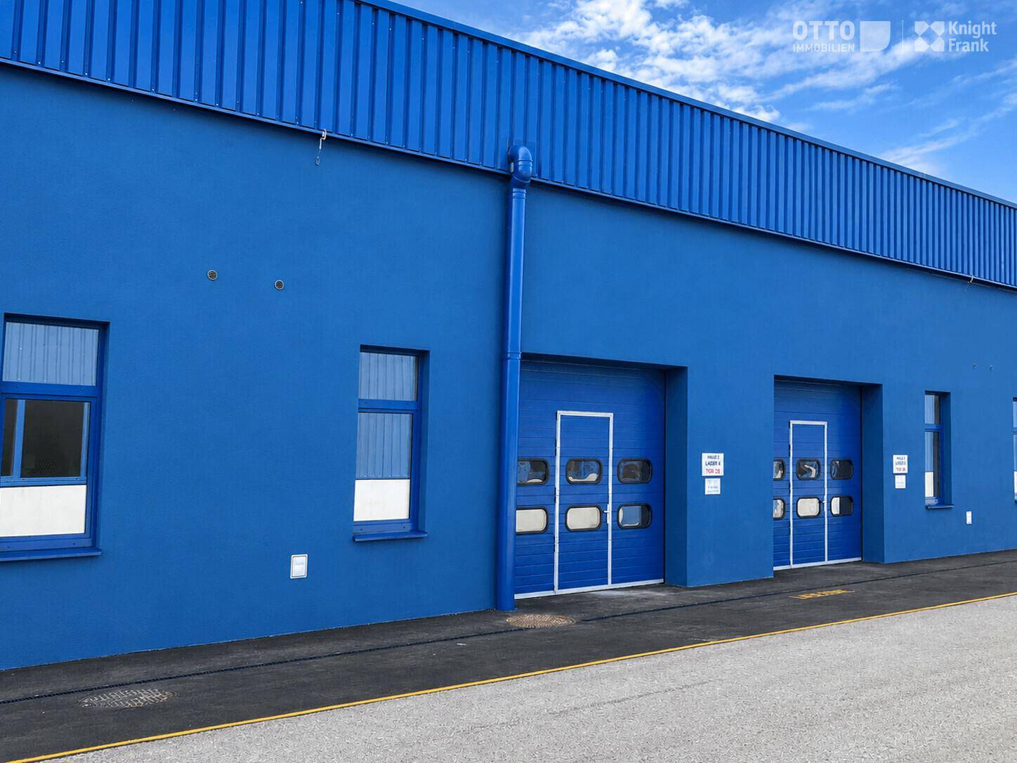 Nahaufnahme der blauen Fassade eines Industriegebäudes mit zwei Rolltoren und Fenstern.