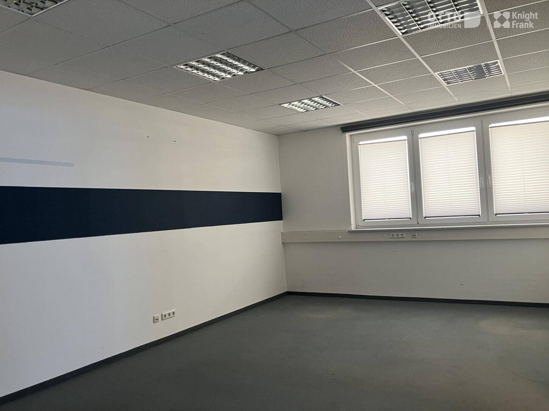 Leeres Büro mit abgehängter Decke, Jalousien an den Fenstern und einem dunklen Streifen an der Wand.