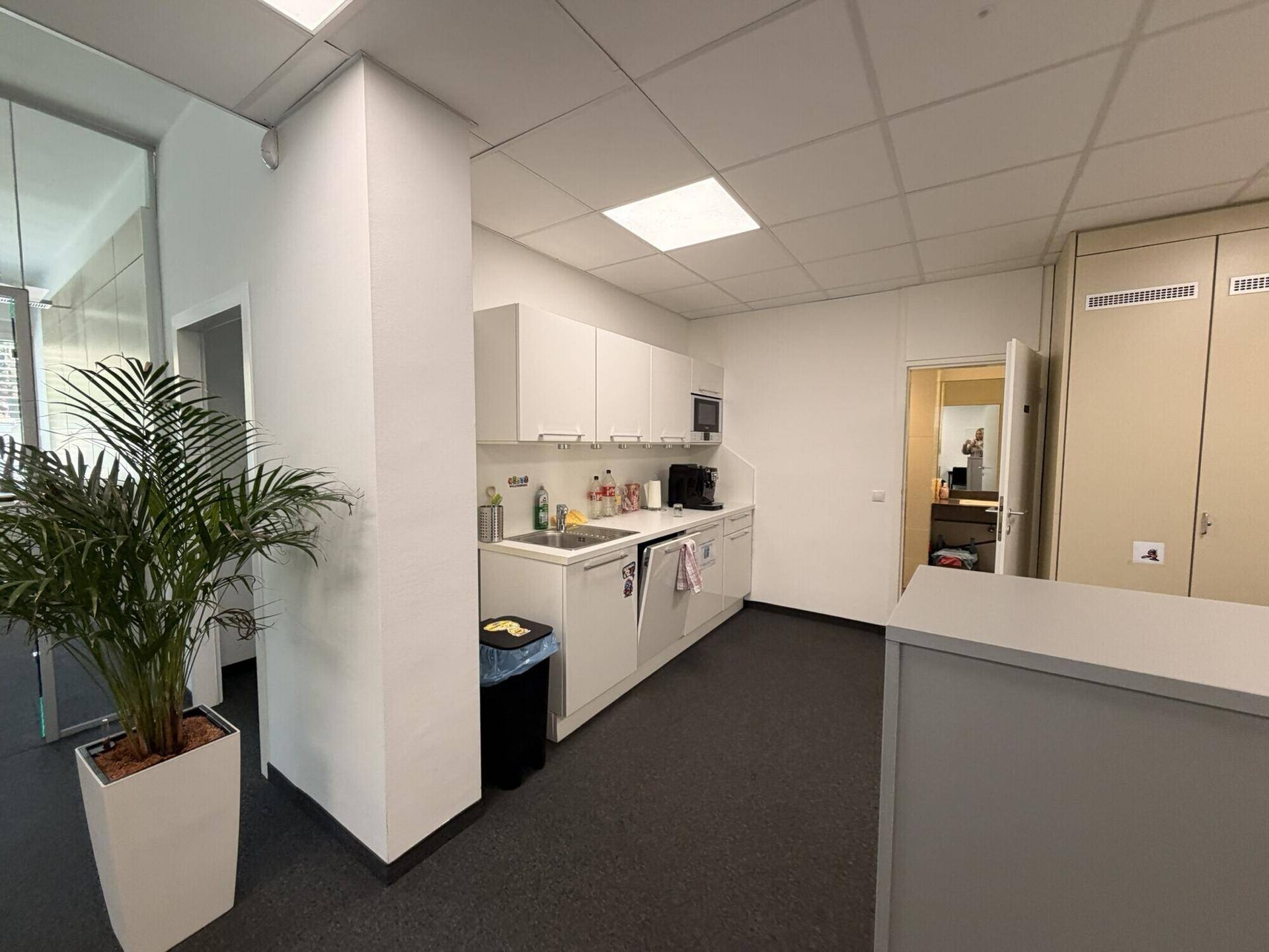 Kleine Teeküche mit weißen Schränken, Spüle und Mikrowelle in einem Bürobereich.