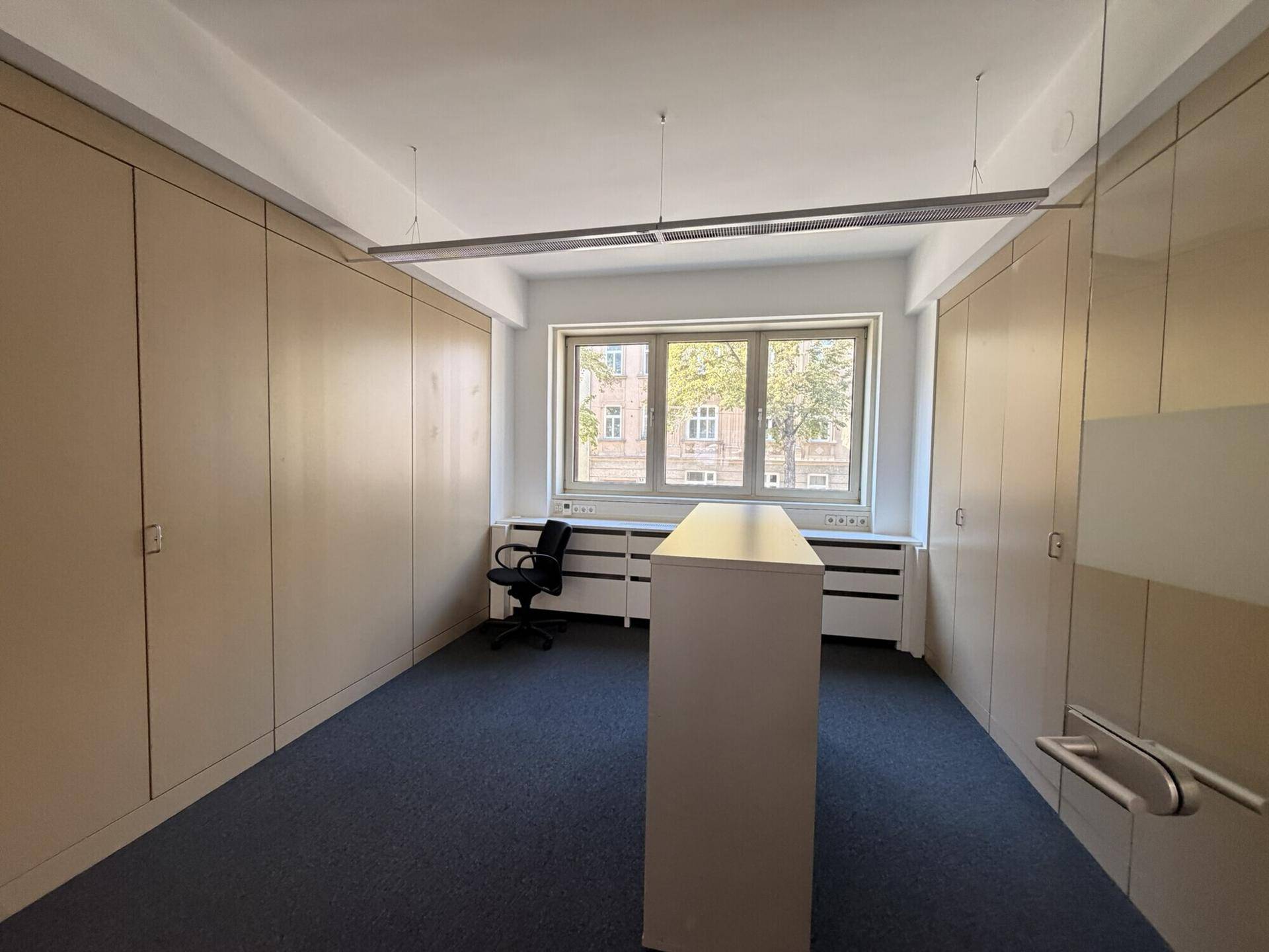 Büroraum mit integrierten Wandschränken, einem zentralen Arbeitstisch und Teppichboden.