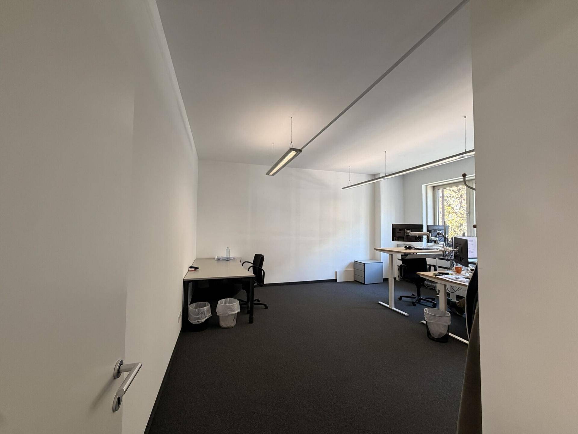 Bürofläche mit mehreren Arbeitsplätzen, Computern und ausreichend Tageslicht durch die Fenster.