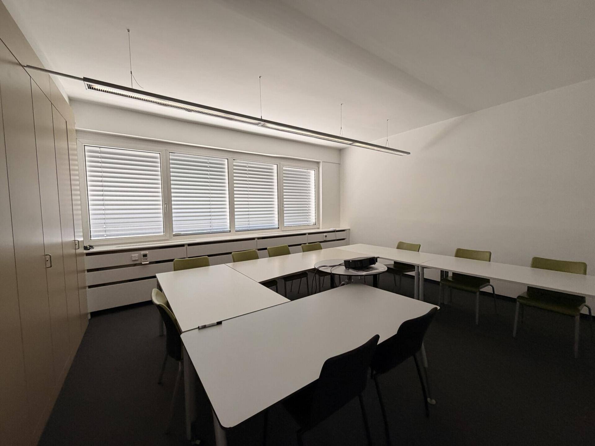 Konferenzraum mit U-förmiger Tischordnung, bequemen Stühlen und einem Projektor für Präsentationen.