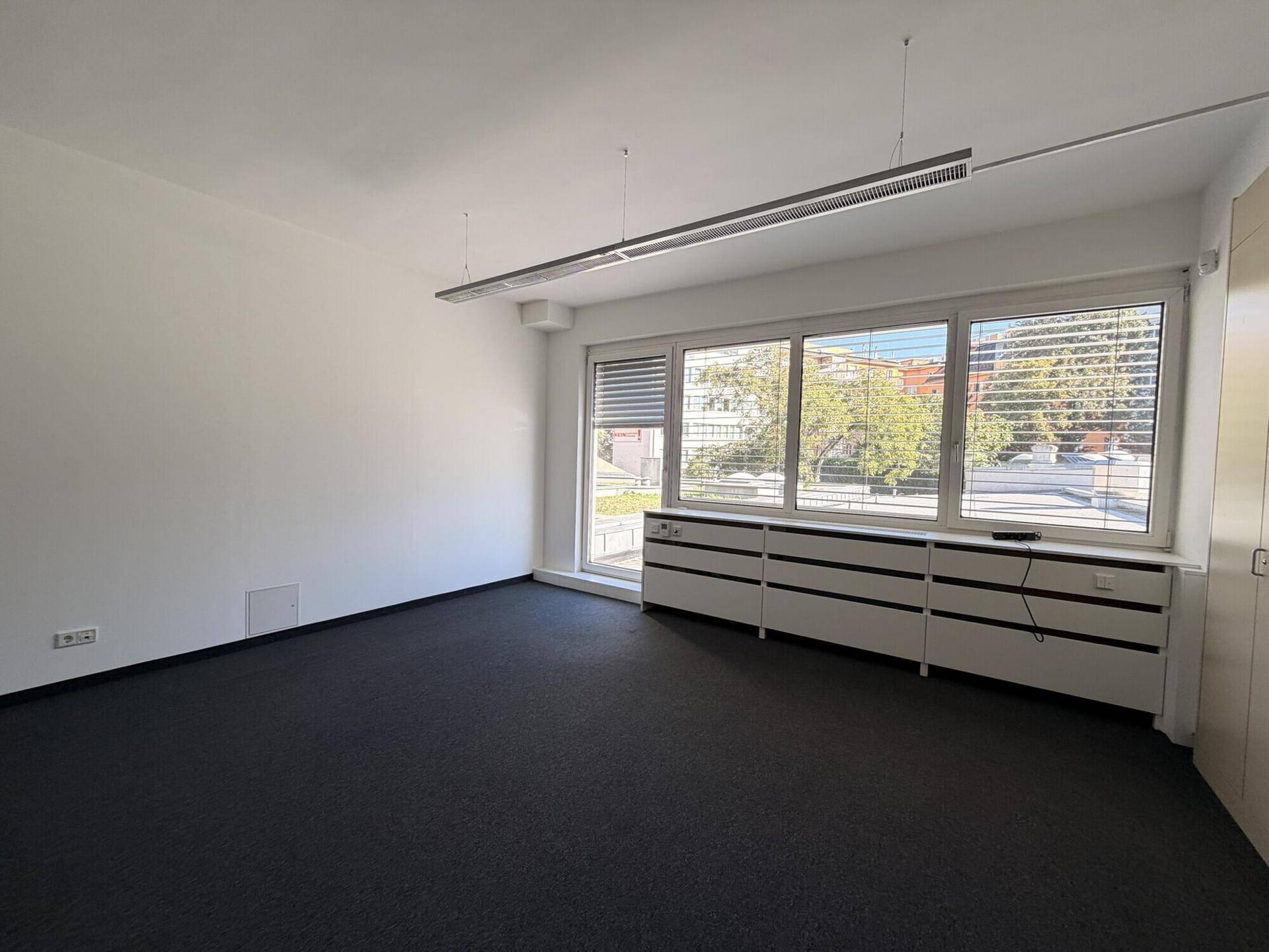 Leerer Büroraum mit großen Fenstern, die viel Tageslicht hereinlassen und einen Zugang nach draußen bieten.