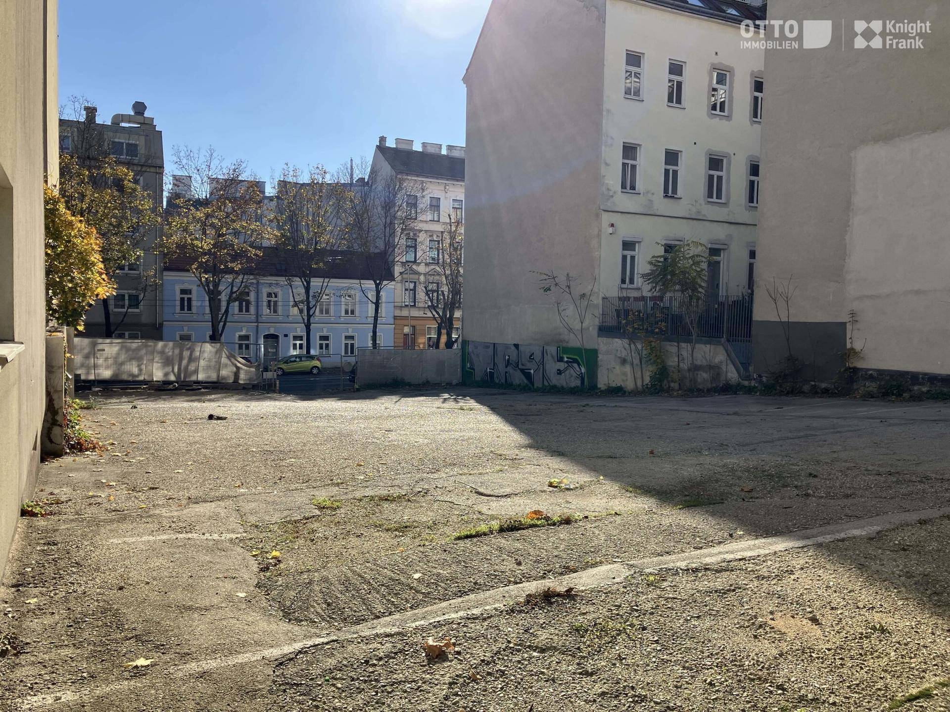 Leeres Grundstück zwischen Gebäuden mit Blick auf die umliegende Bebauung unter blauem Himmel.