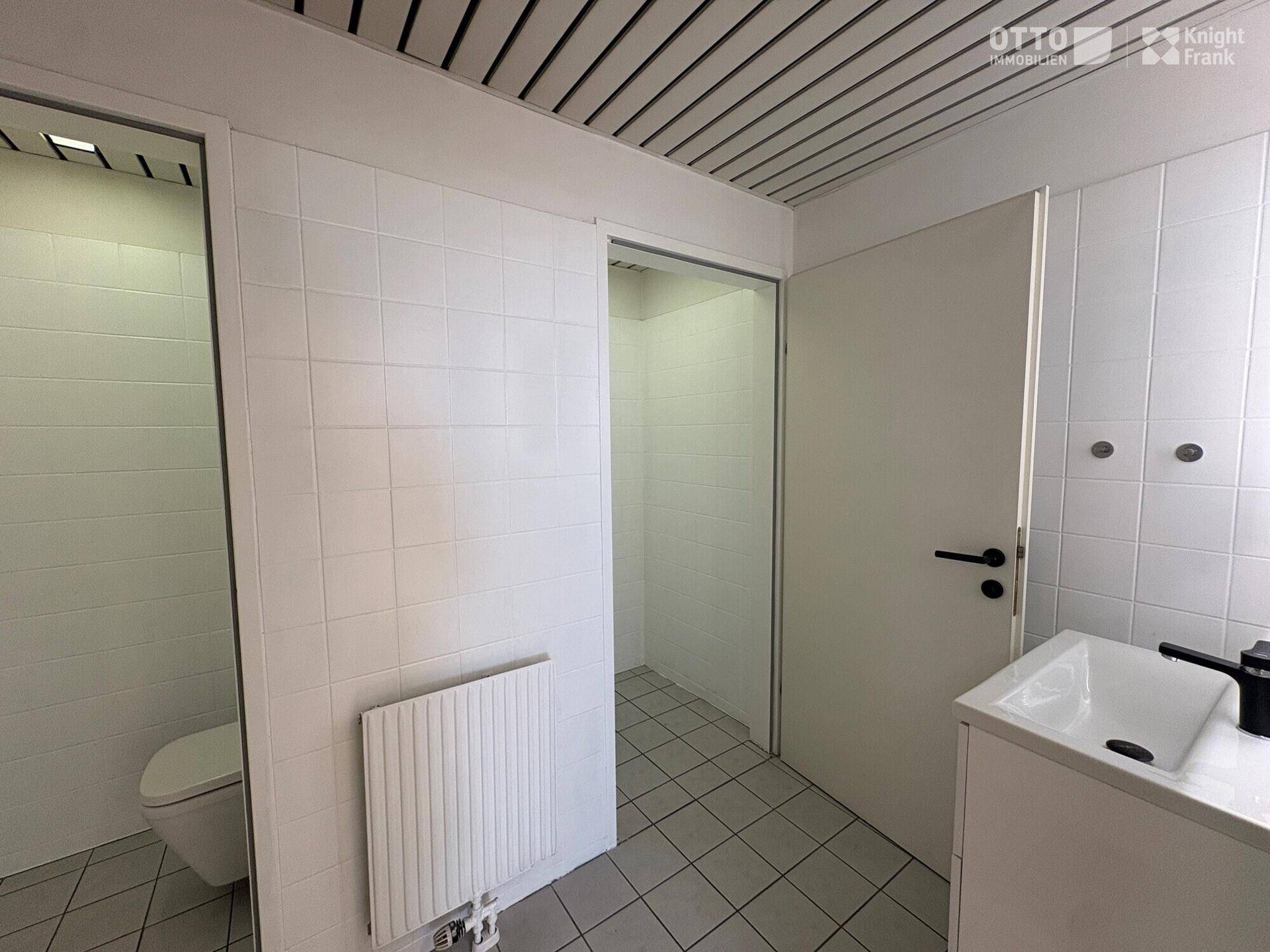 Modern gefliestes Badezimmer mit WC, Waschbecken und Duschbereich, in gutem Zustand.
