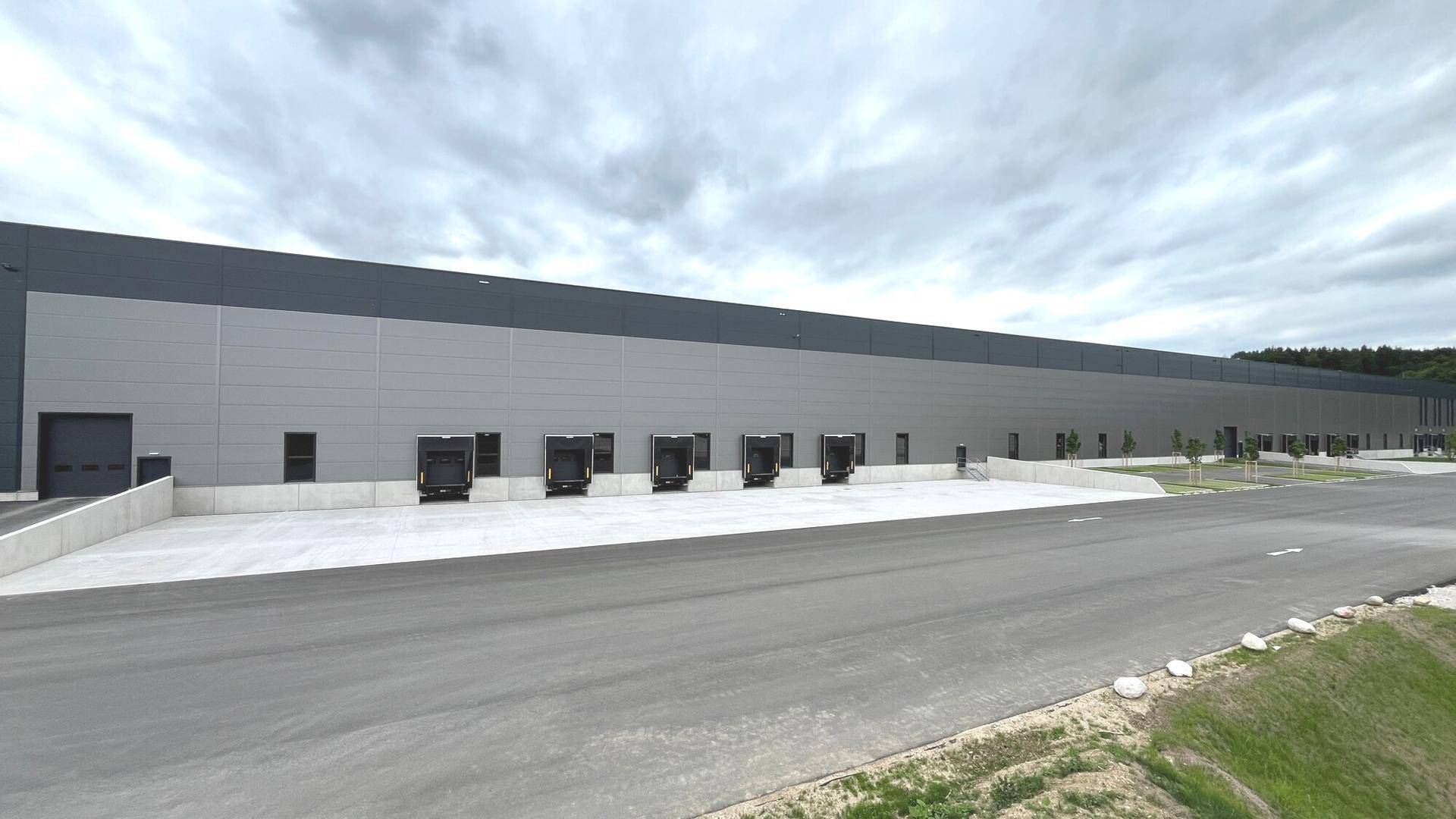 Lange Fassade des modernen Logistikzentrums mit zahlreichen Laderampen und weitläufigem Vorplatz.