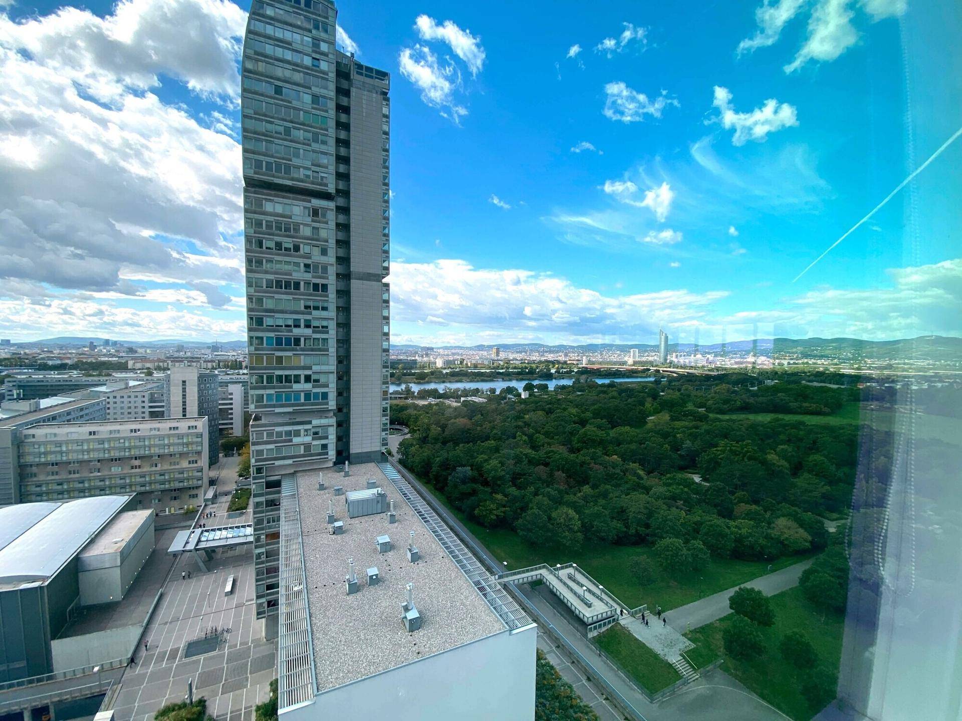 Panoramablick von einem Hochhaus auf einen Fluss, eine grüne Parklandschaft und die Skyline der Stadt.