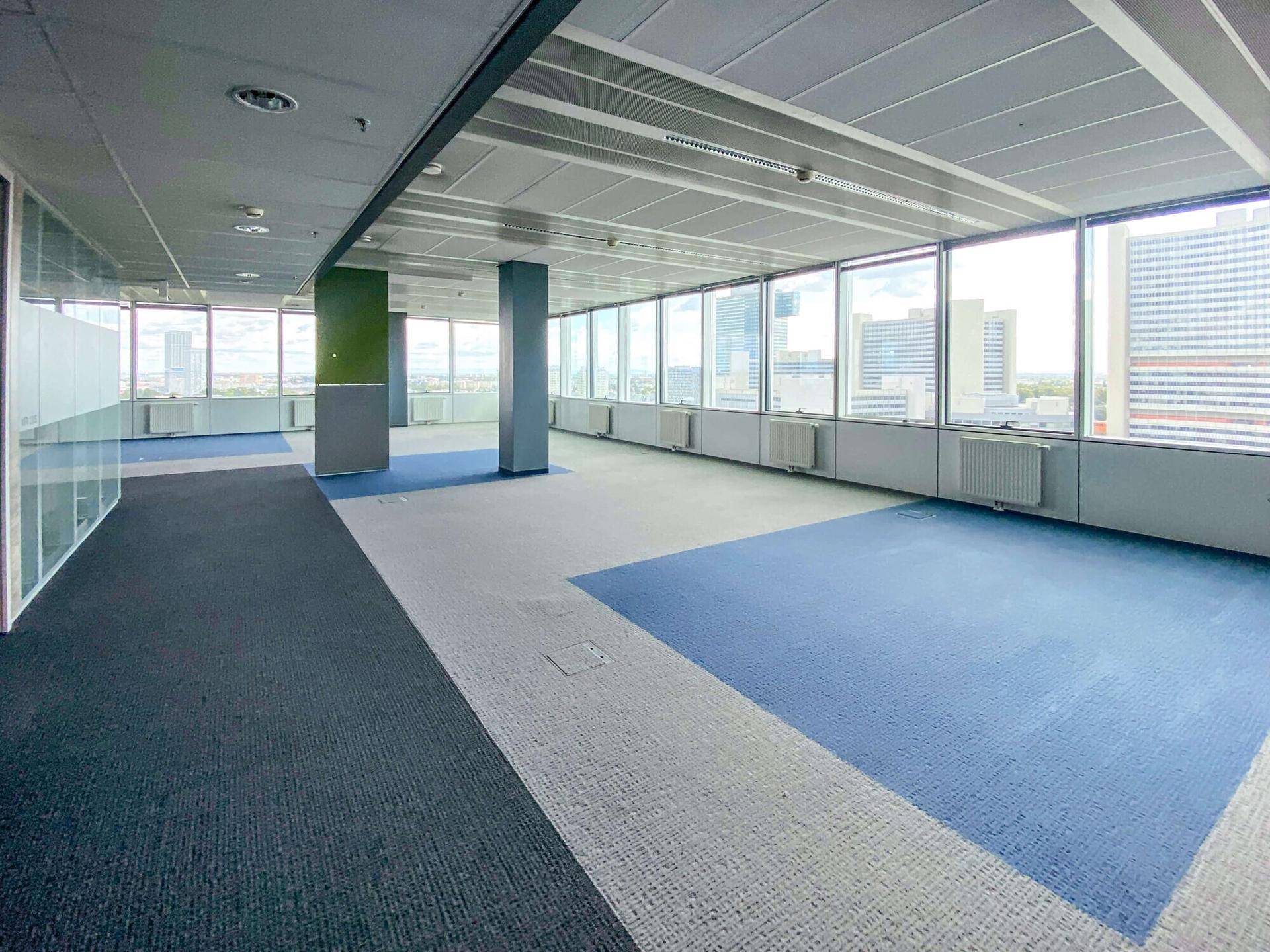 Helles, offenes Büro mit Teppichboden, Heizkörpern und Panoramablick auf die Stadt.