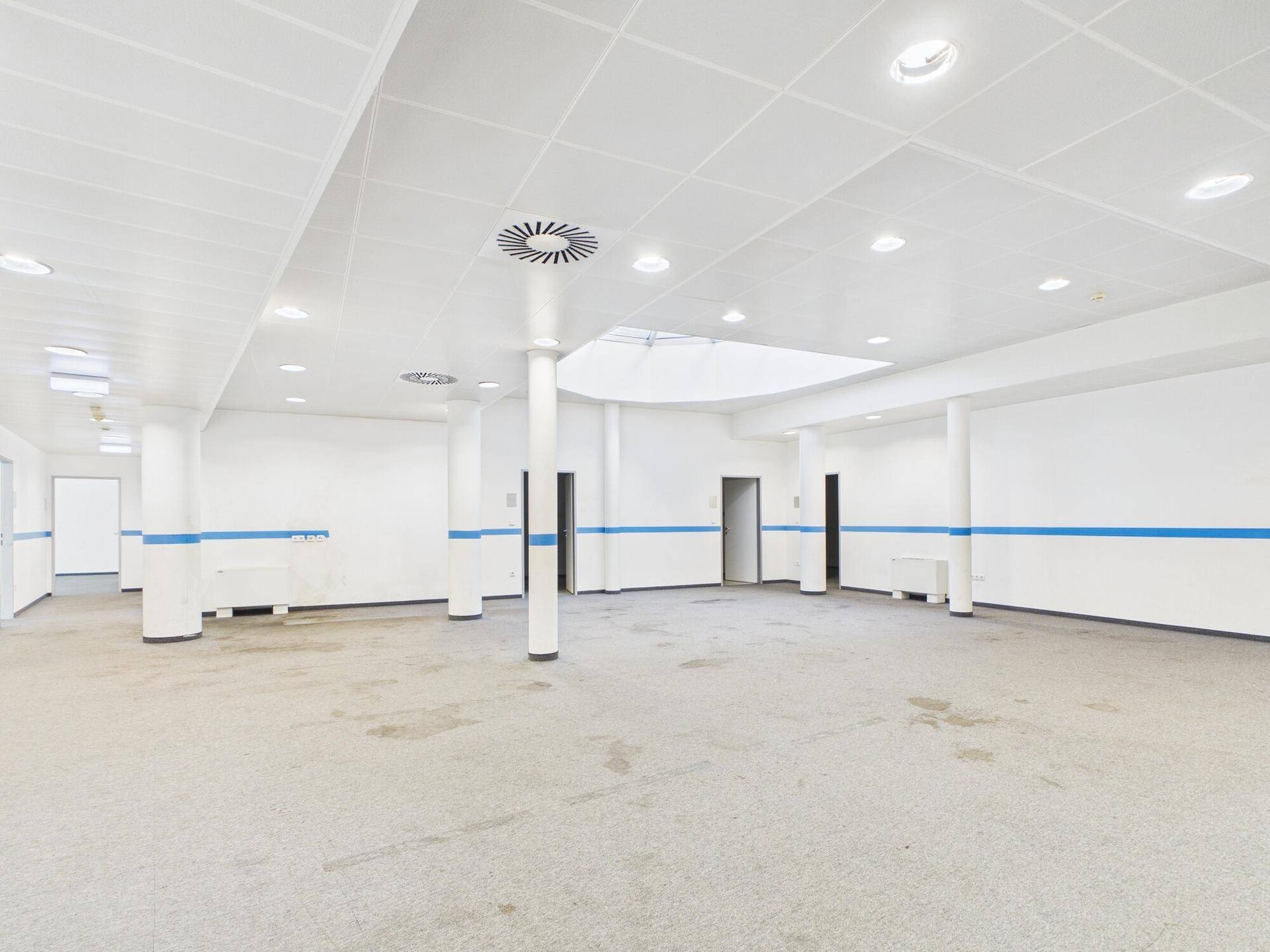 Großer, offener Bereich mit Säulen, abgehängter Decke und blauen Akzentstreifen an den Wänden.